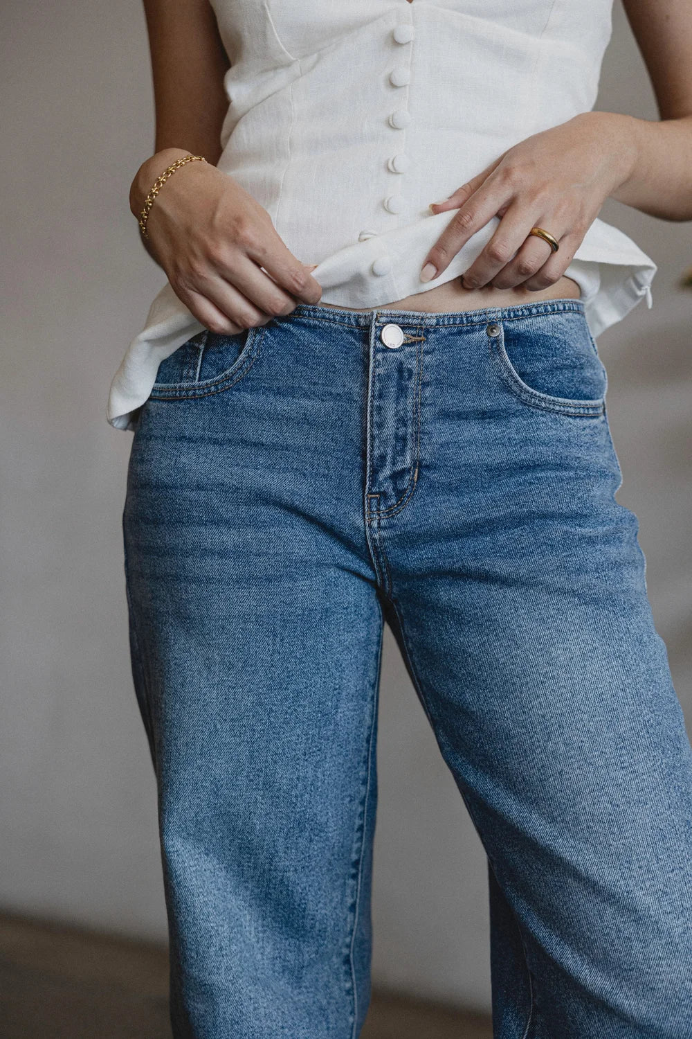 Person wearing blue jeans and a white shirt with a neutral background
