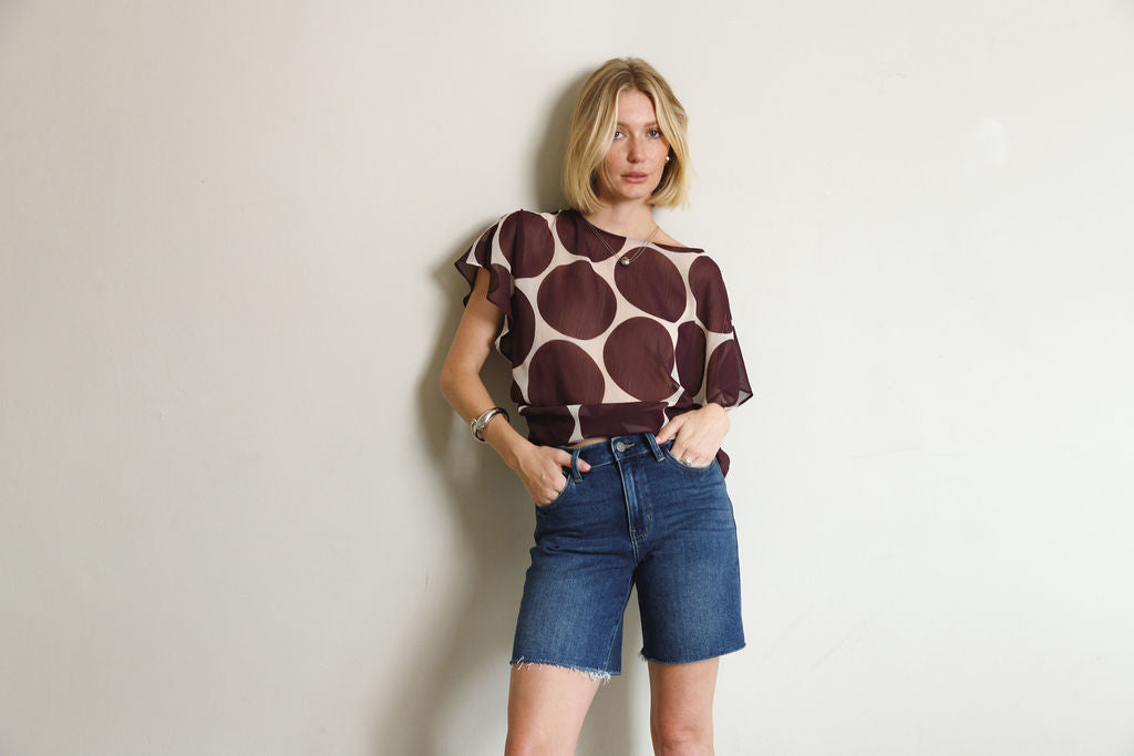 Woman wearing a patterned top and denim shorts against a plain background