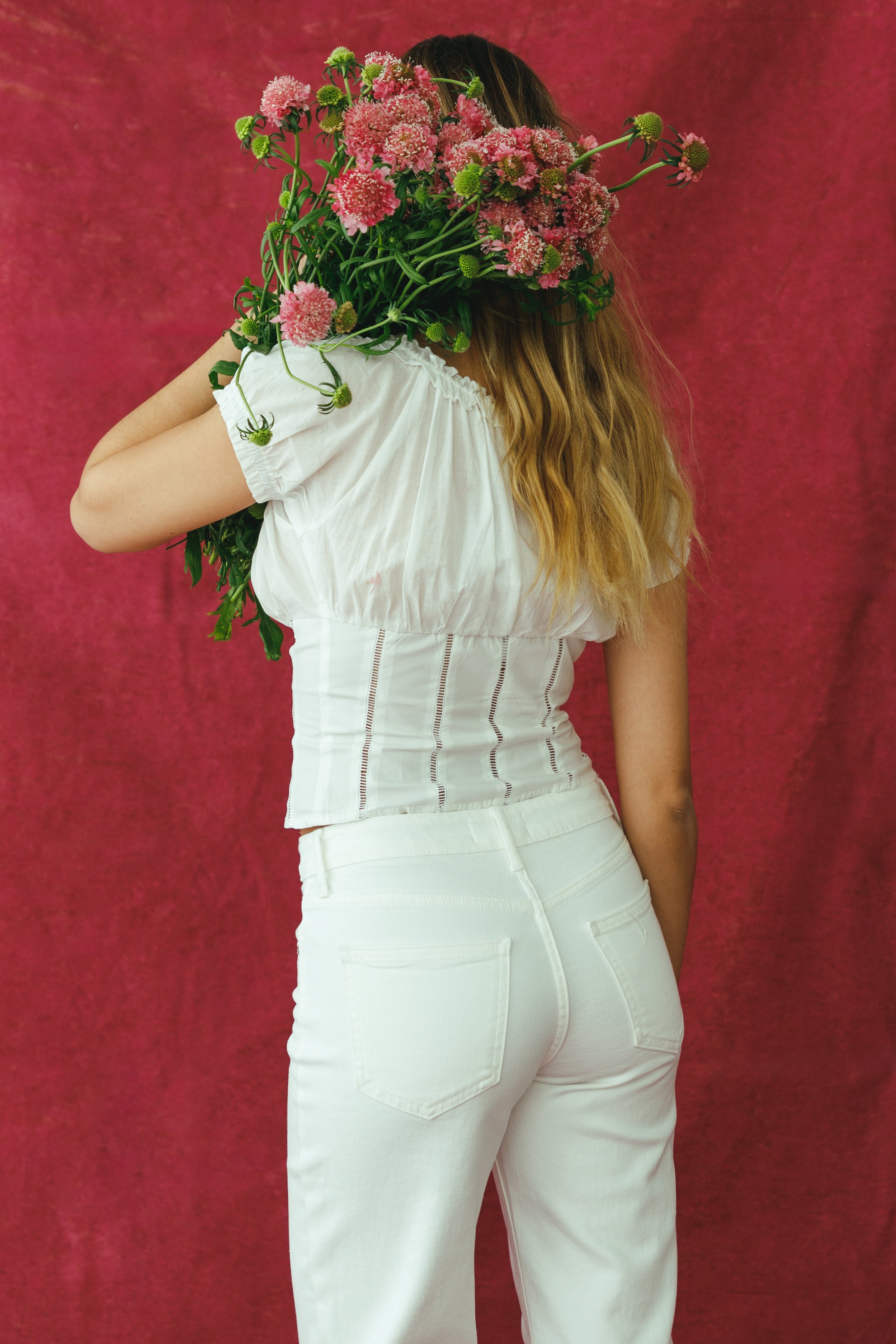 Person wearing a white outfit holding pink flowers against a red background