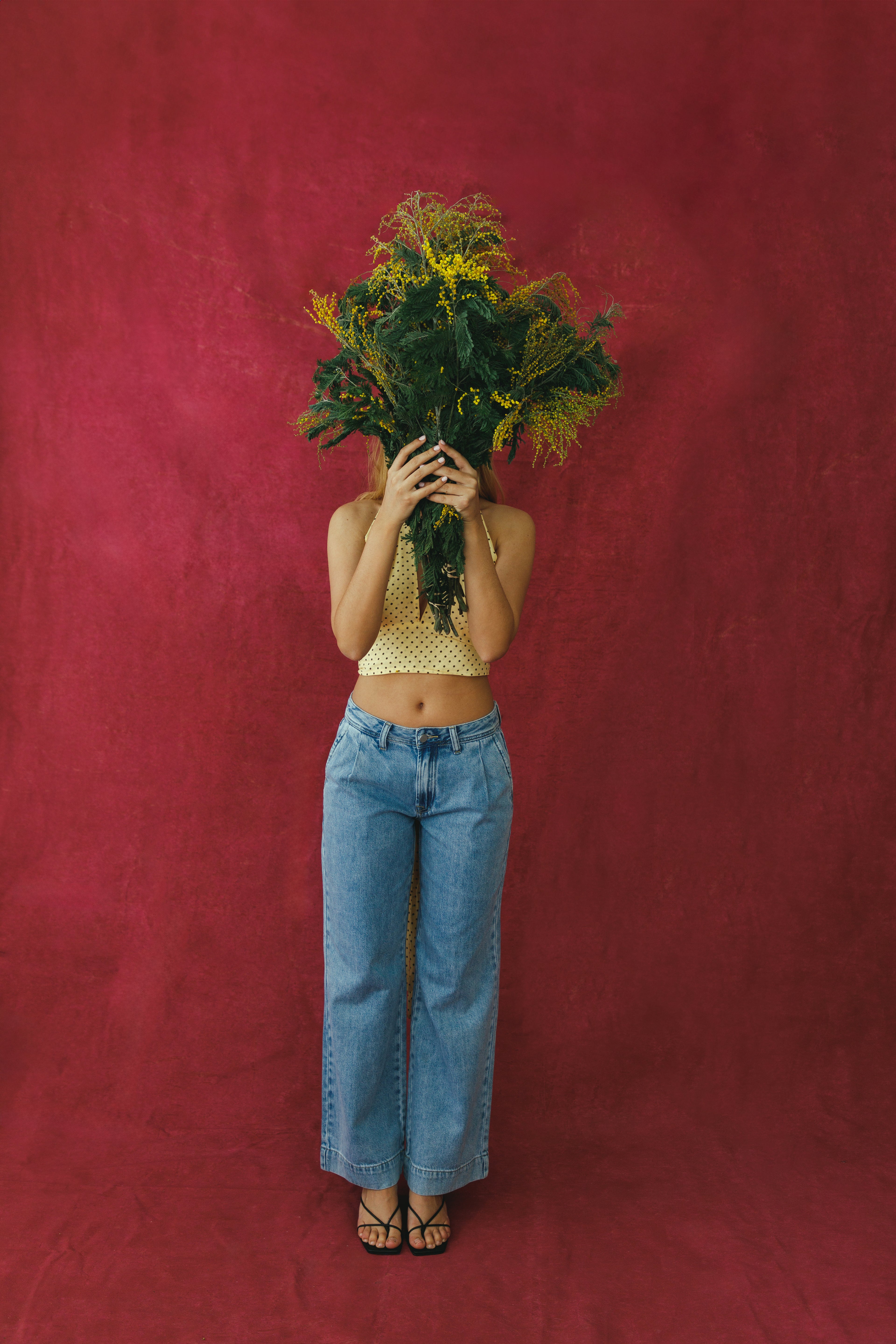Person holding a bouquet of flowers in front of their face against a red background