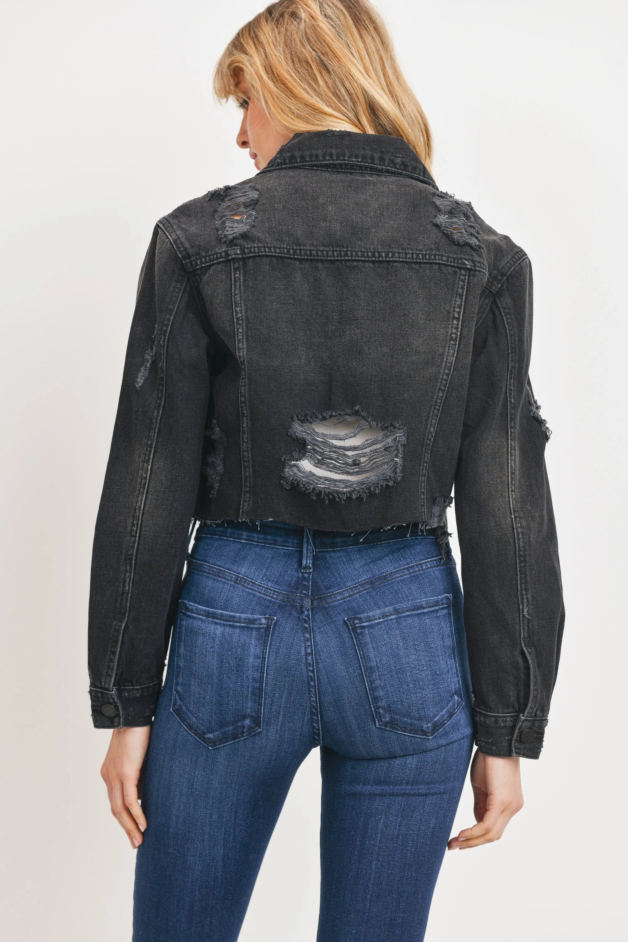 Person wearing a black denim jacket with visible distressing on a plain background
