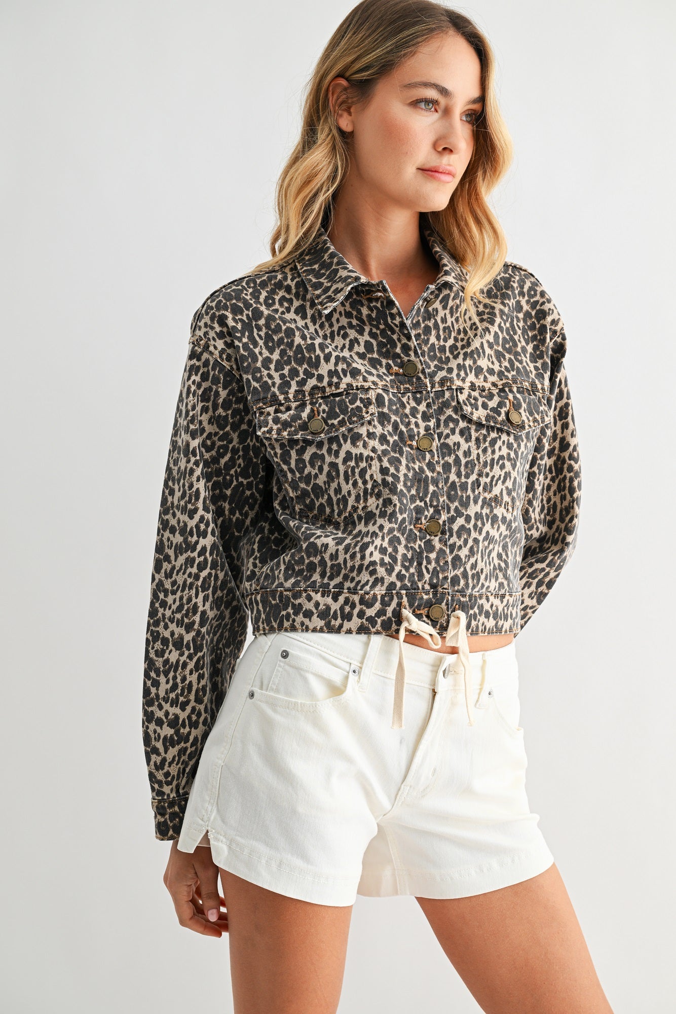 Woman wearing a leopard print shirt and white shorts on a plain background