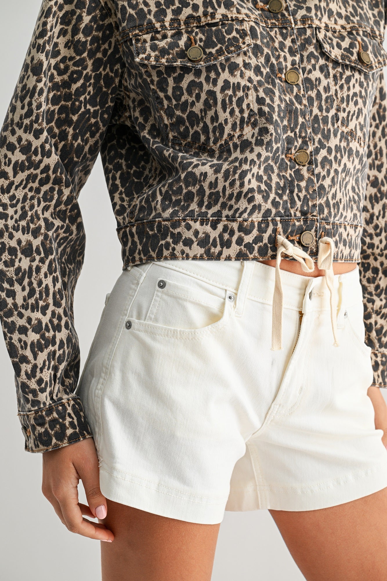 Person wearing a leopard print jacket and white shorts on a plain background