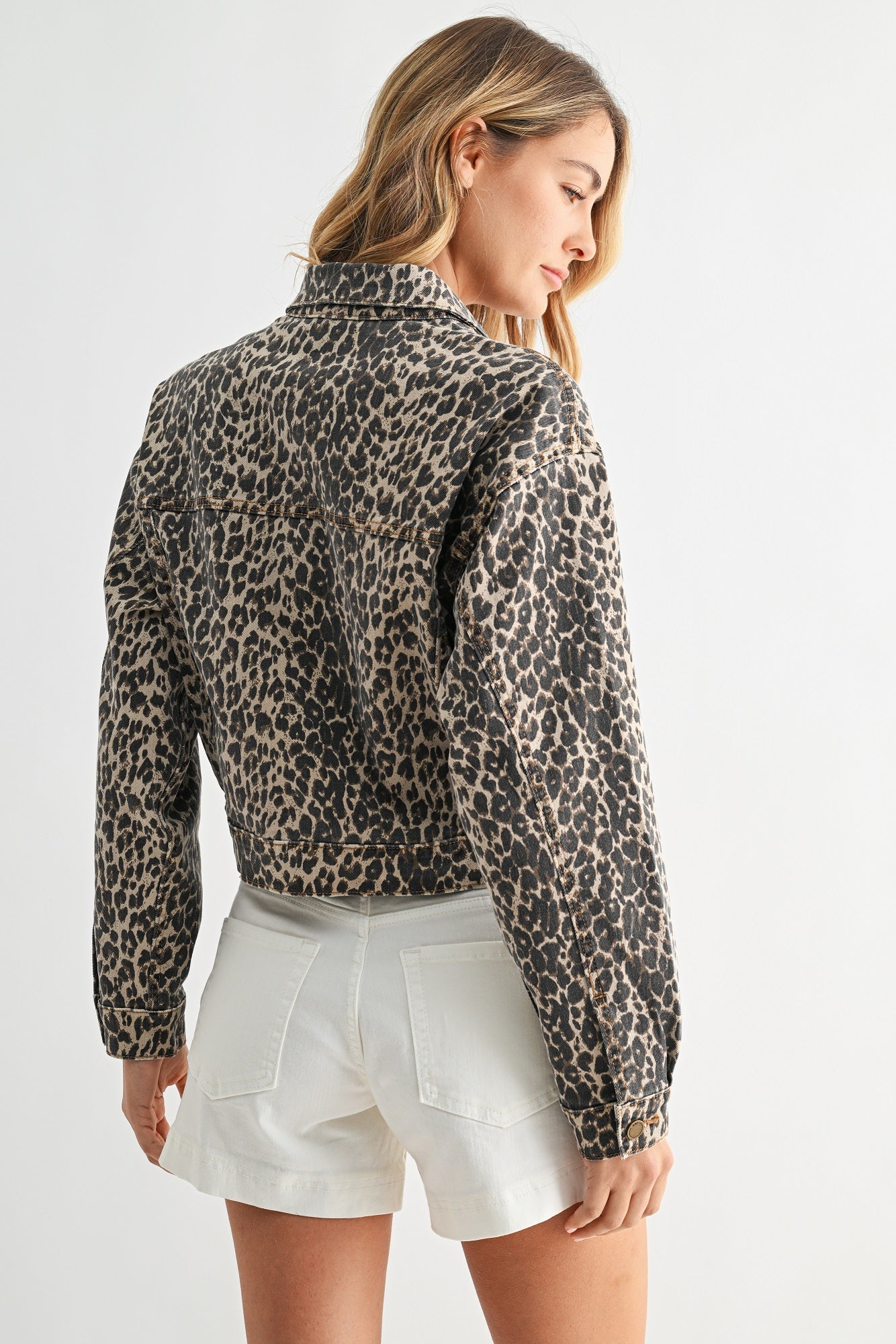 Woman wearing a leopard print jacket and white shorts on a plain background