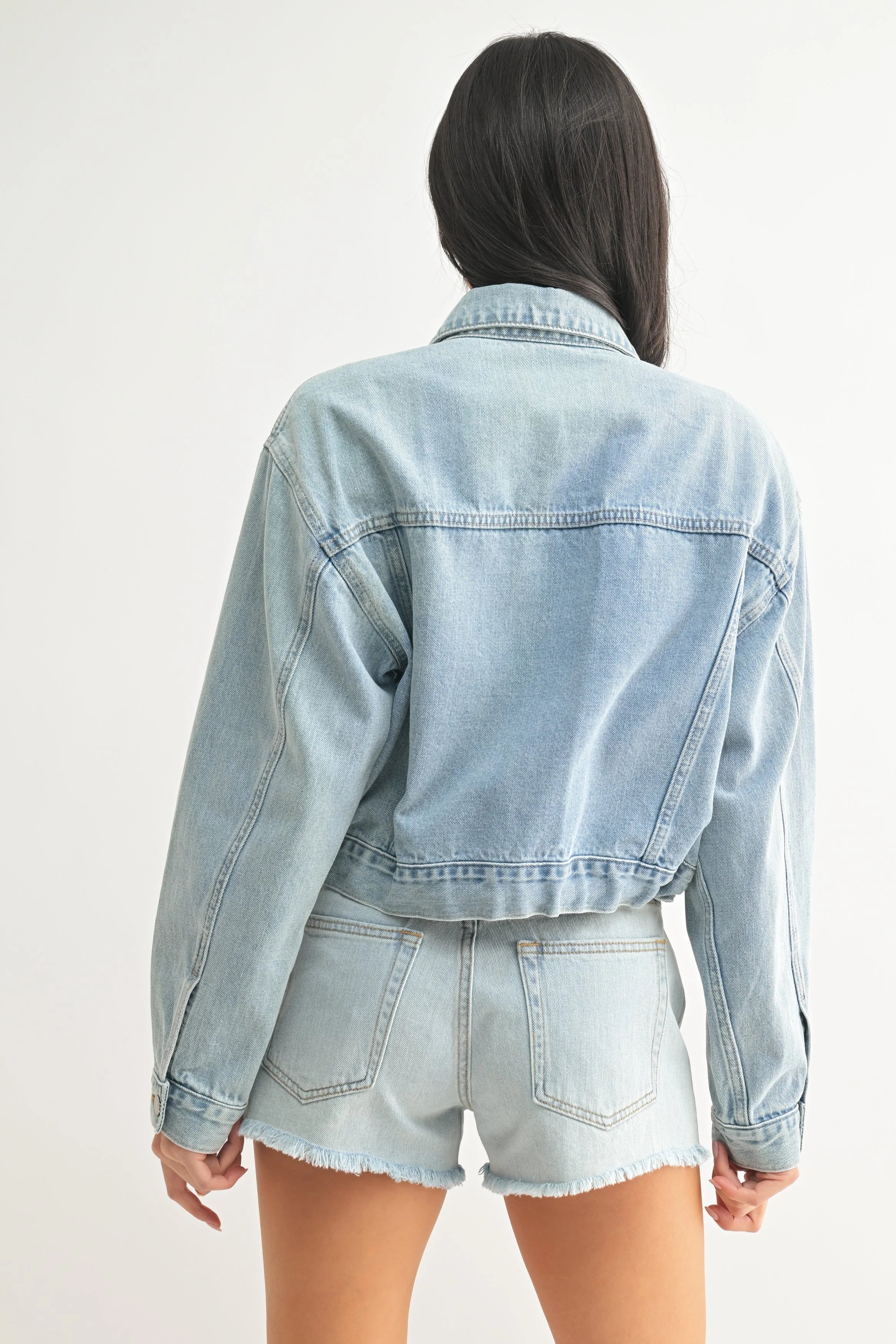 Person wearing a light blue denim jacket and shorts on a white background