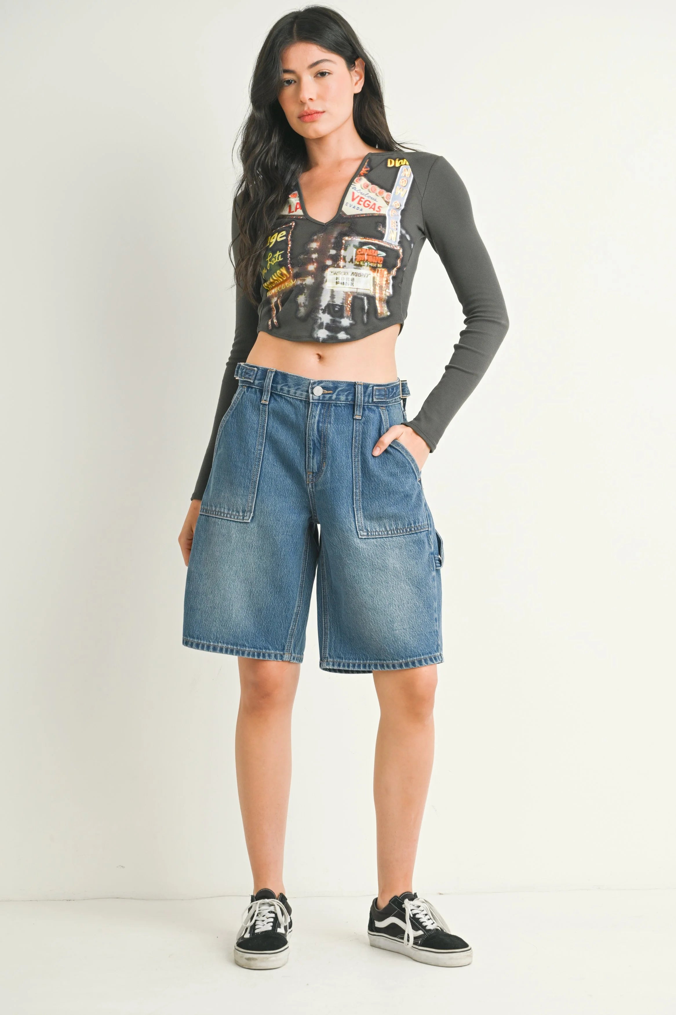 Woman wearing a long-sleeve graphic top and denim shorts on a white background