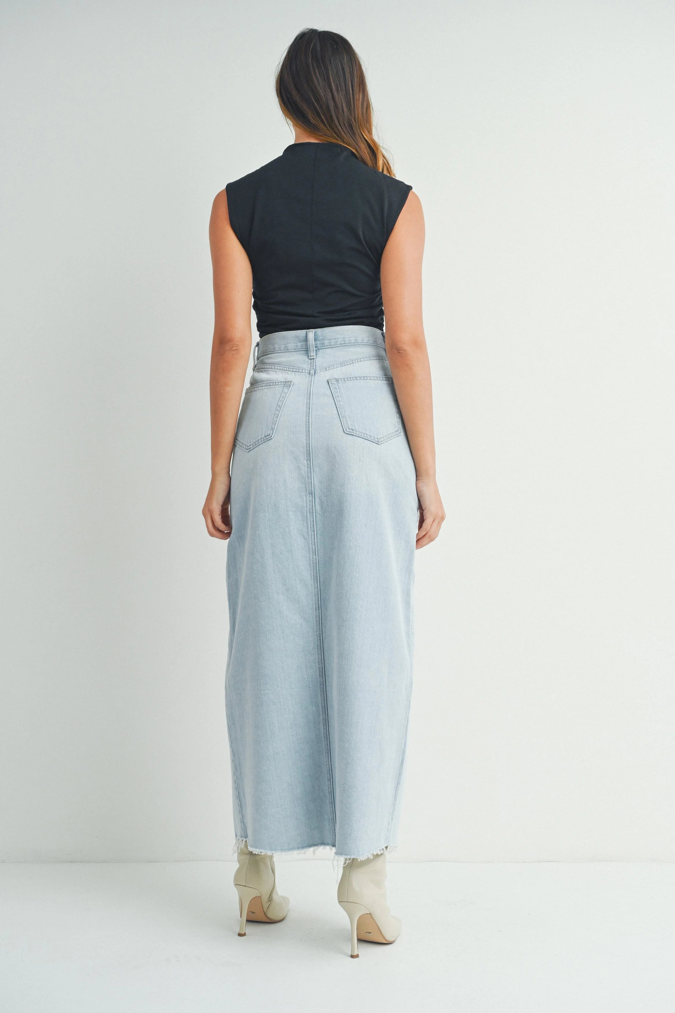 Woman wearing a black sleeveless top and light blue denim skirt on a white background