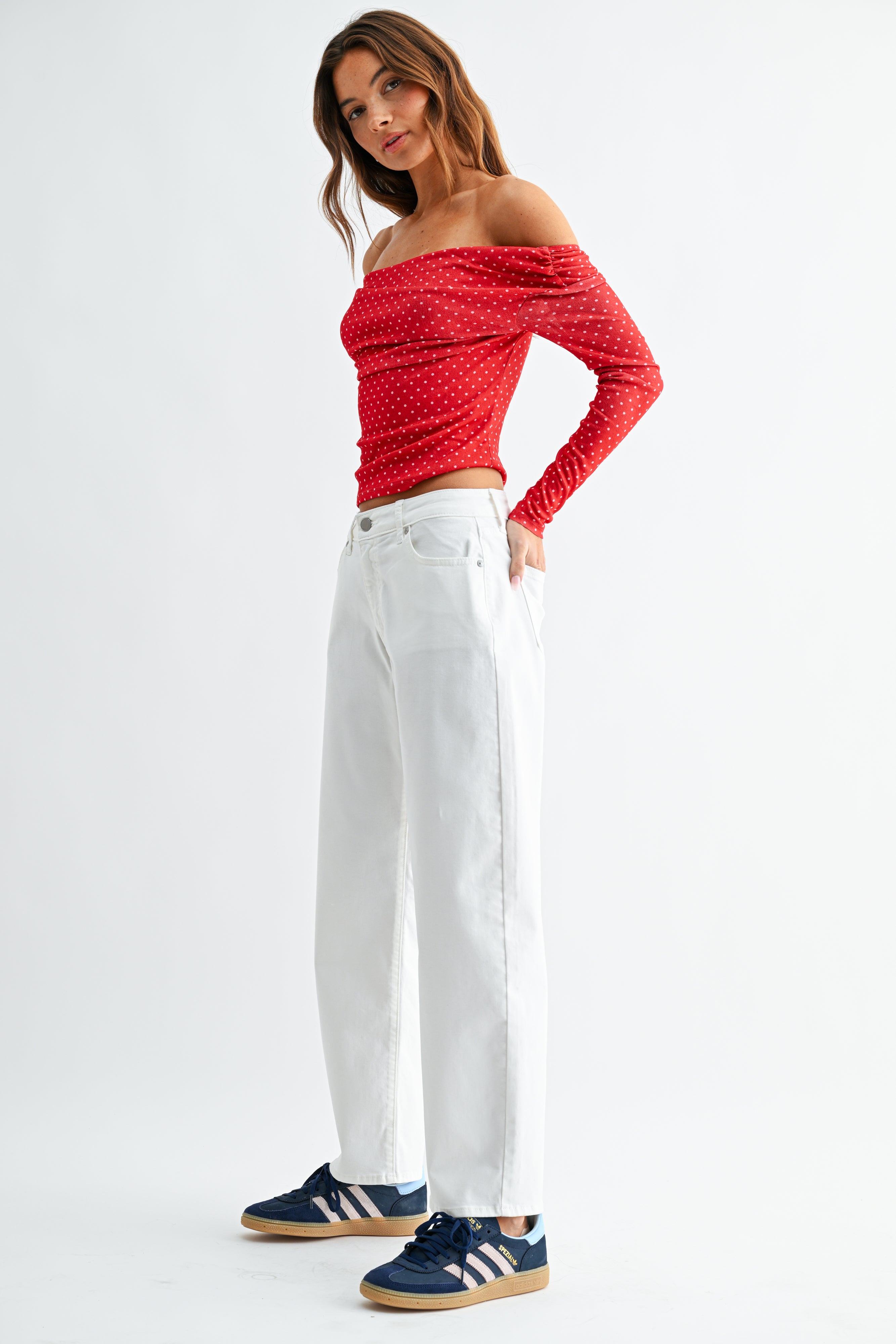 Woman wearing a red off-shoulder top and white pants on a white background