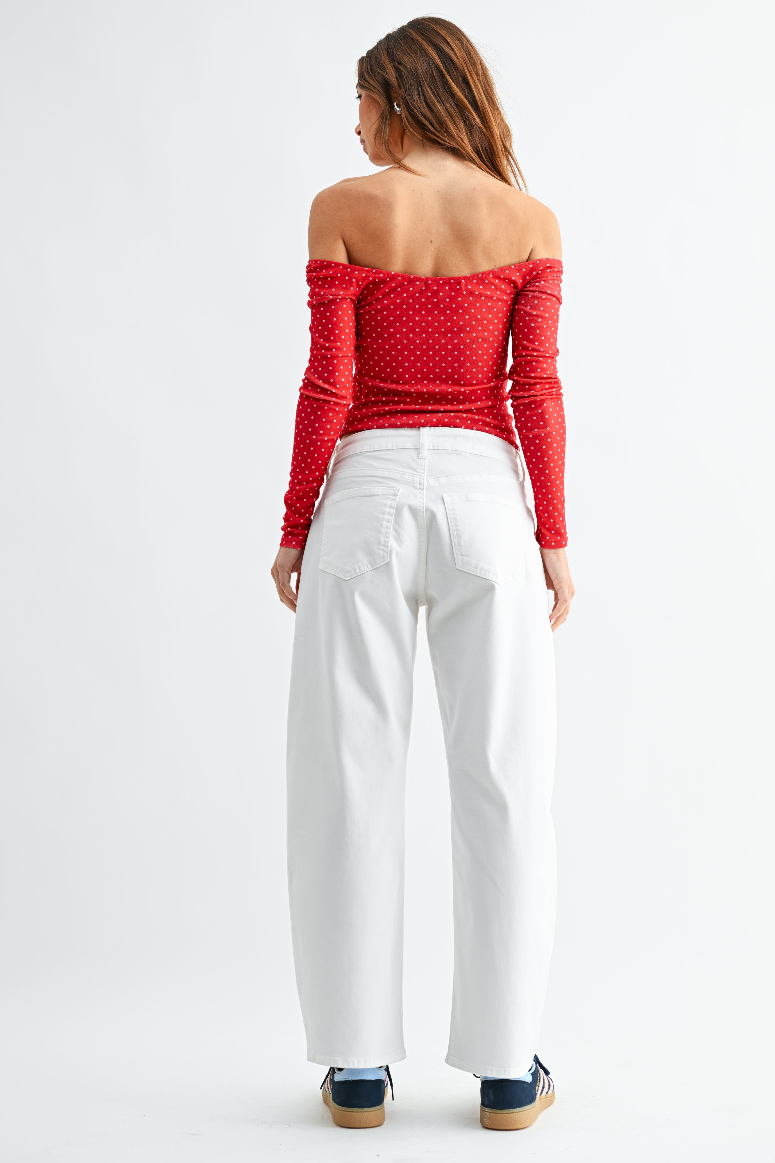 Woman wearing a red polka dot top and white pants on a white background