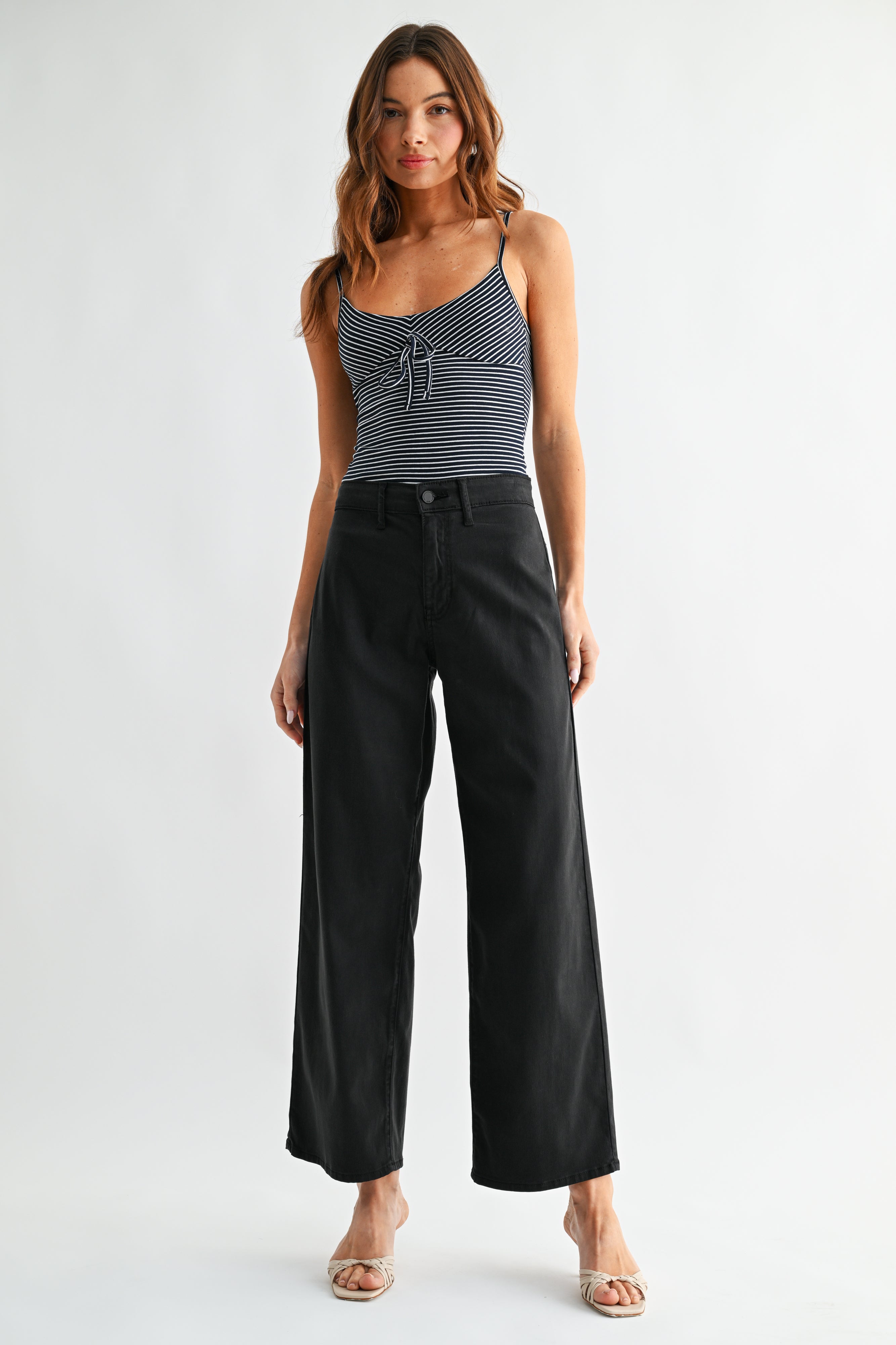 Woman wearing a striped tank top and black wide-leg pants on a white background