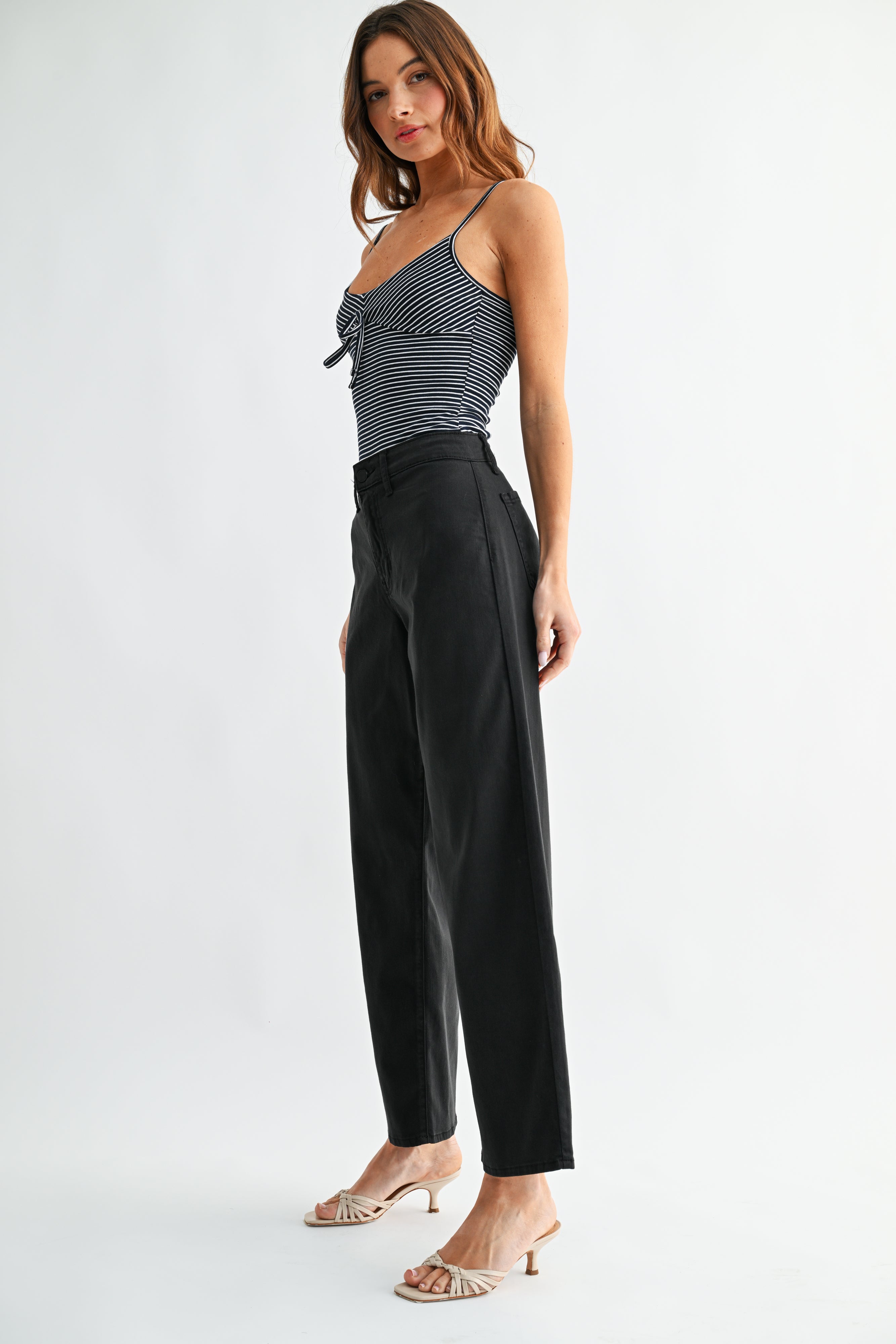 Woman wearing a striped top and black high-waisted pants on a white background
