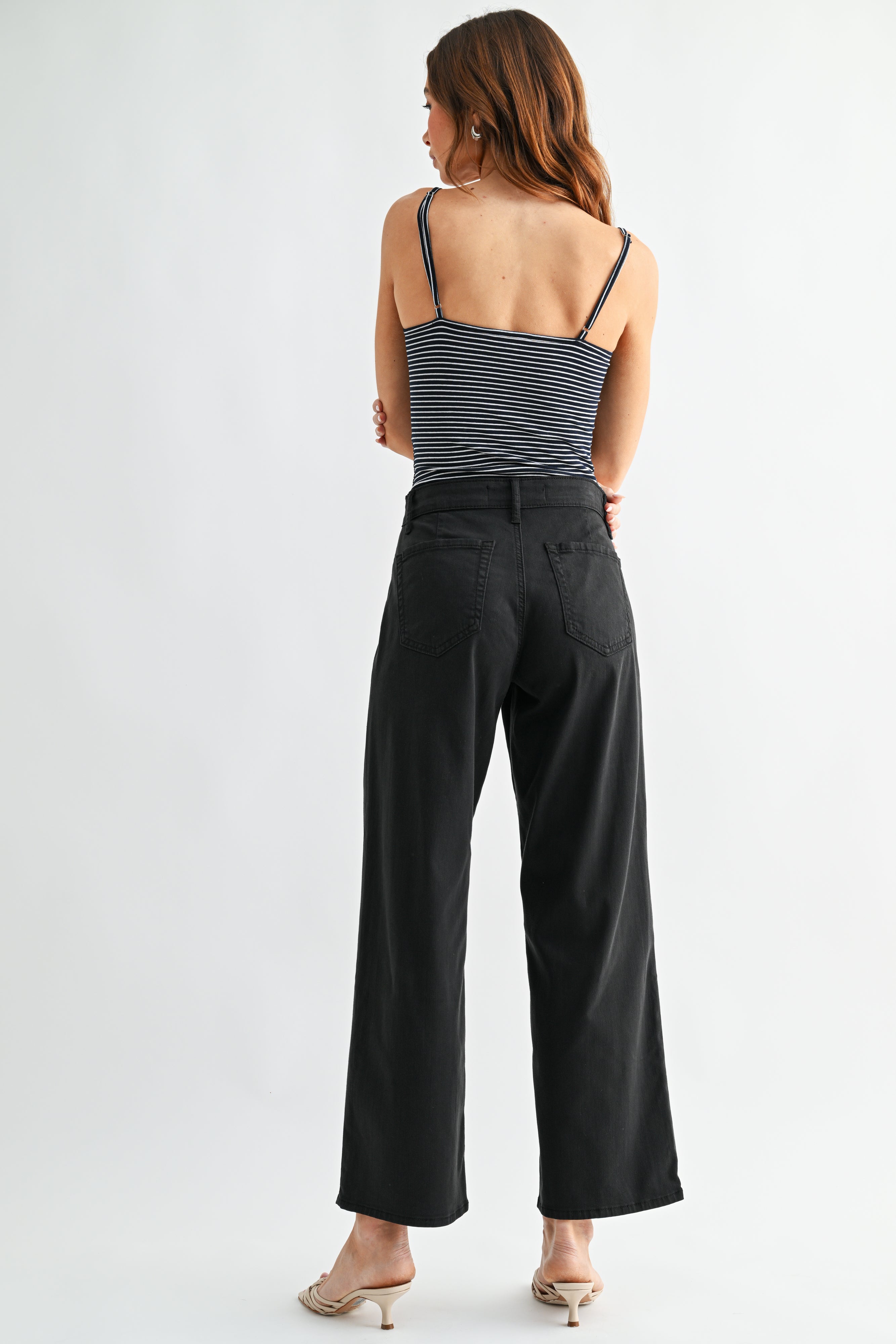 Woman wearing a striped tank top and black wide-leg pants on a white background
