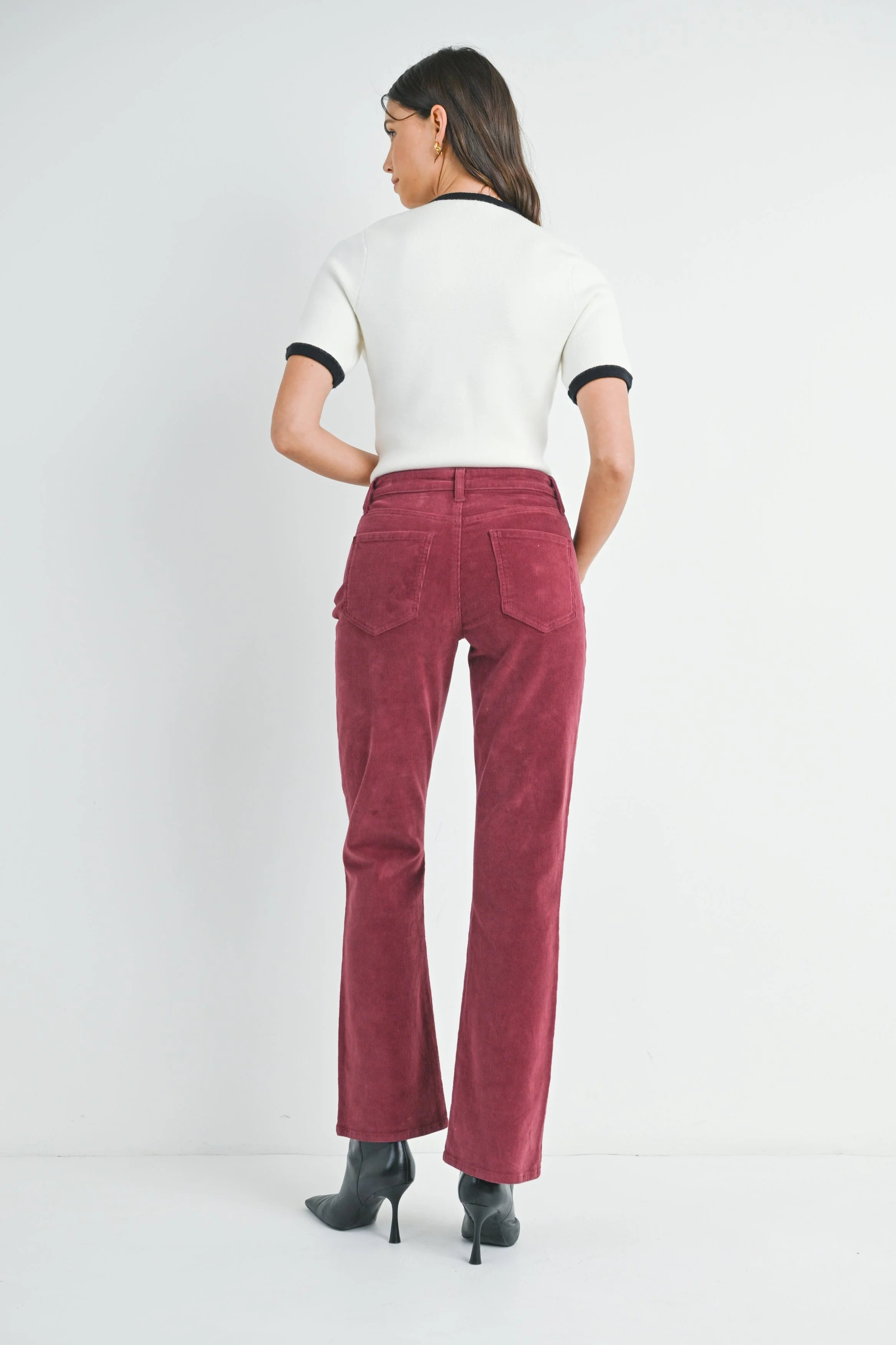 Person wearing a white top with black trim and red corduroy pants on a white background