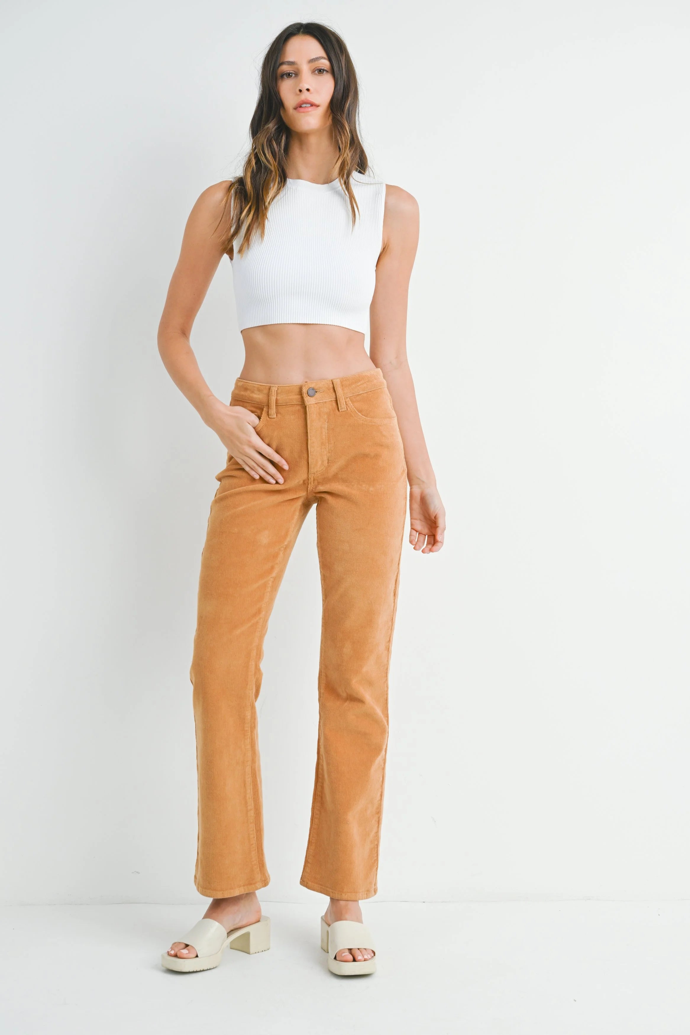 Woman wearing a white sleeveless top and tan pants on a white background