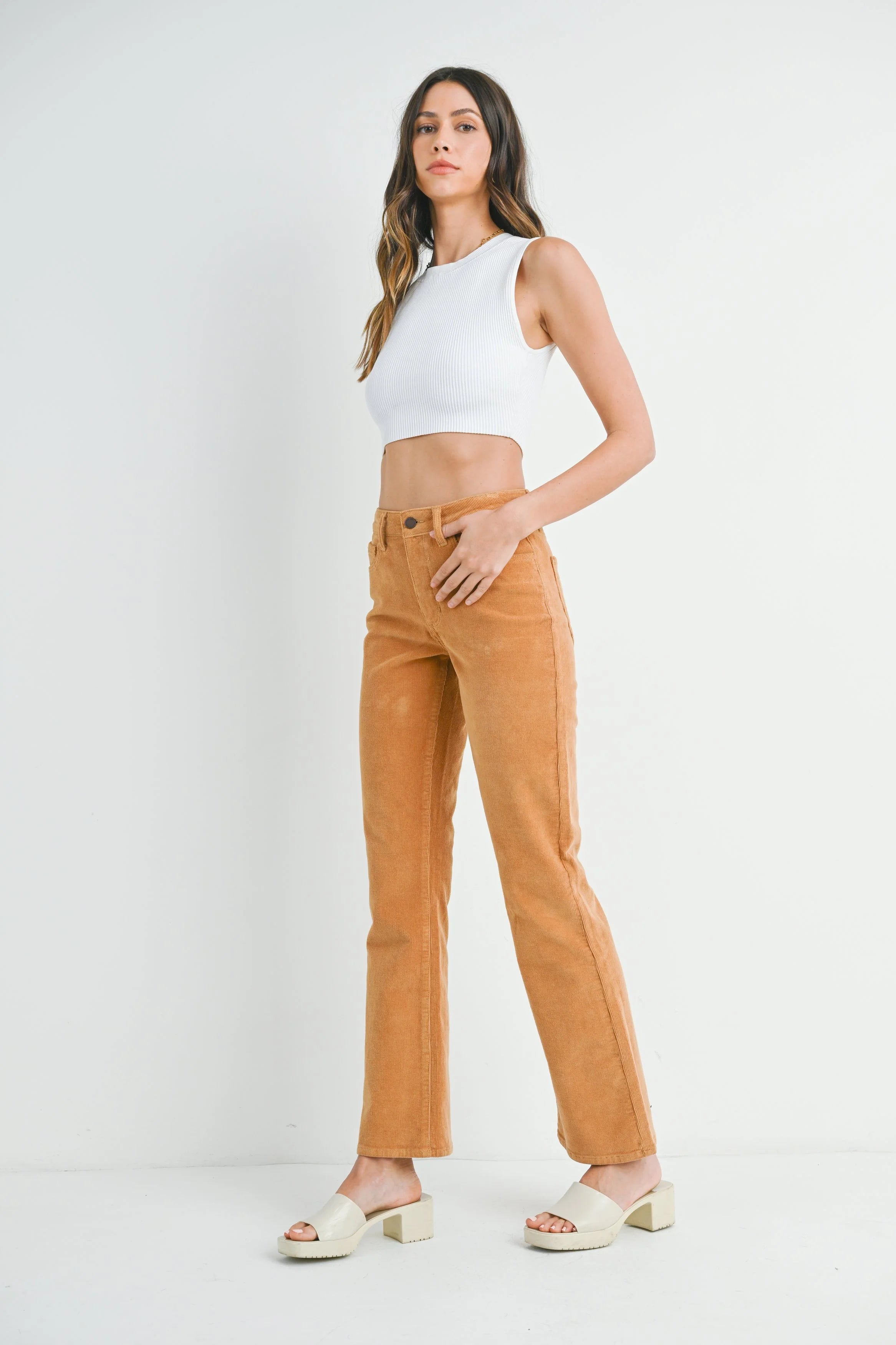 Woman wearing a white sleeveless top and tan pants on a white background