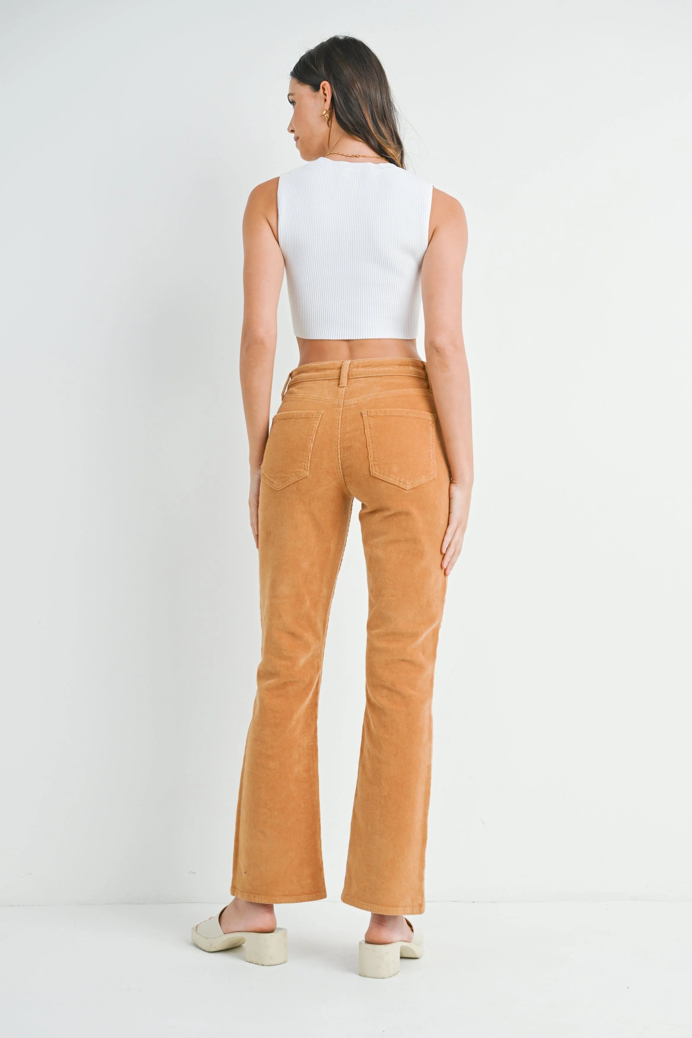 Woman wearing a white sleeveless top and brown corduroy pants on a white background