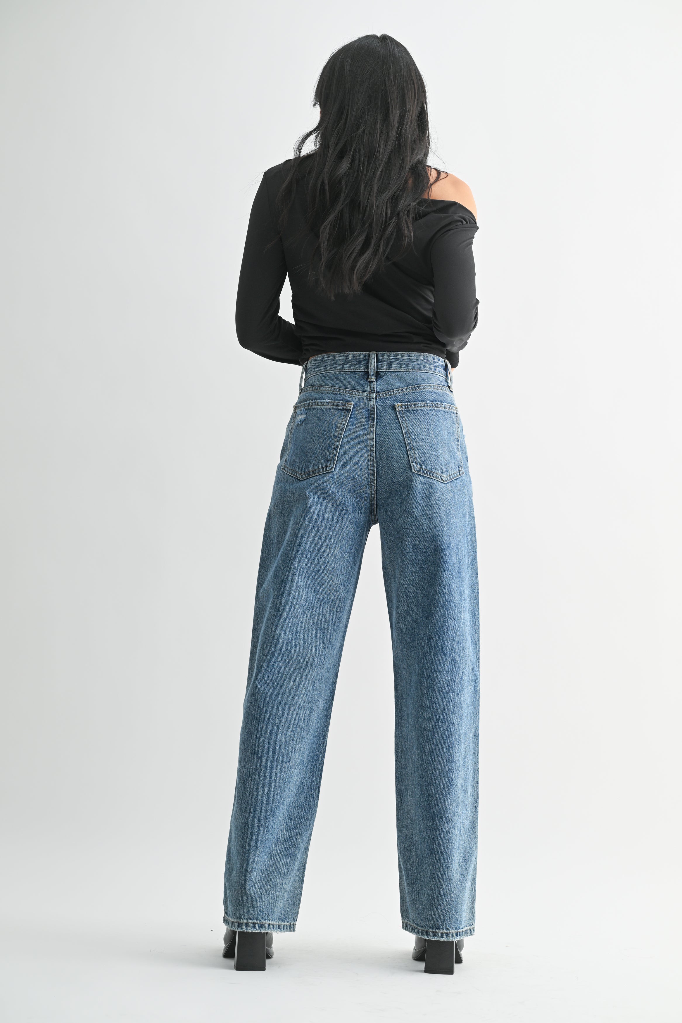 Person wearing blue jeans and a black top on a white background