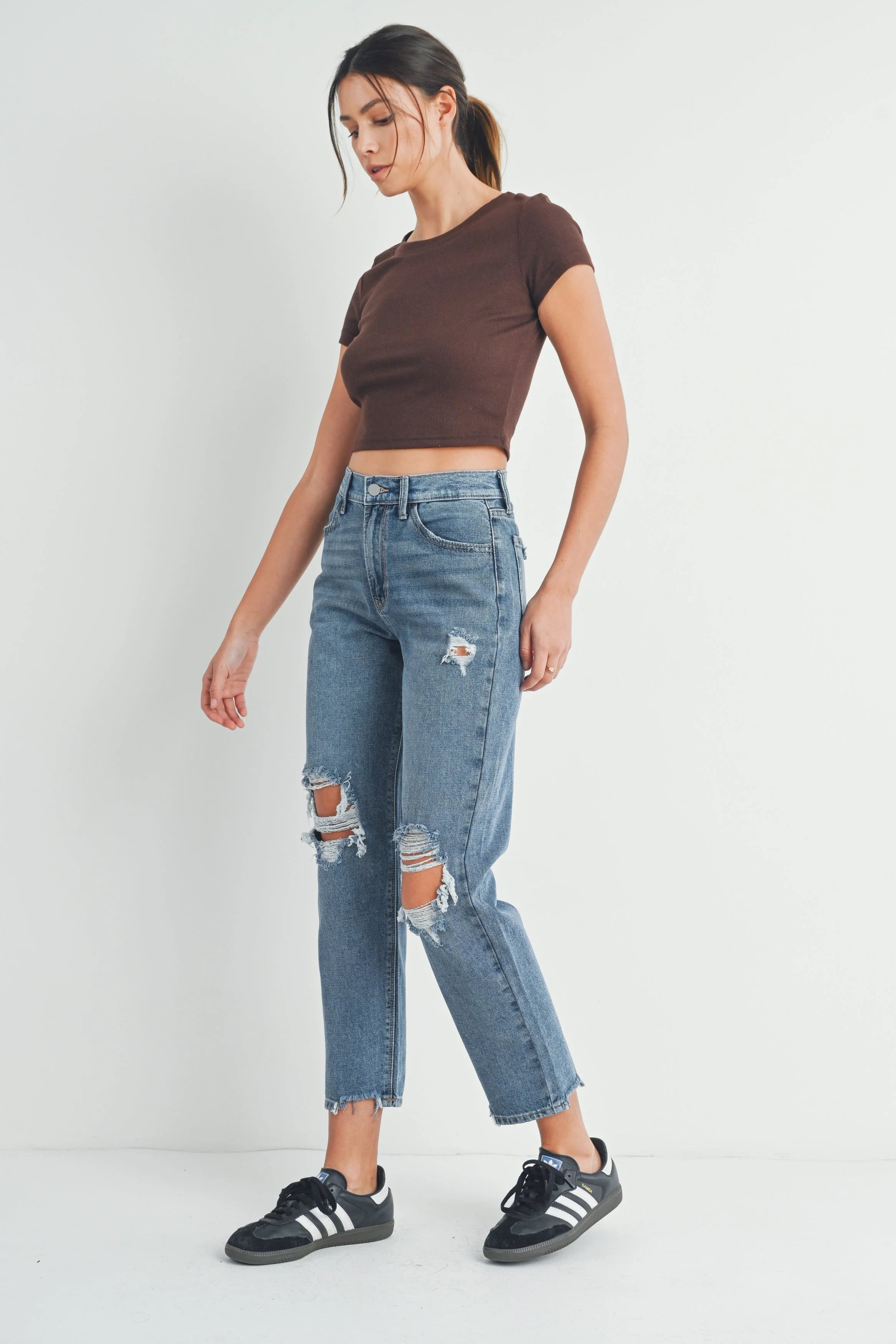 Woman wearing a brown crop top and blue ripped jeans on a white background
