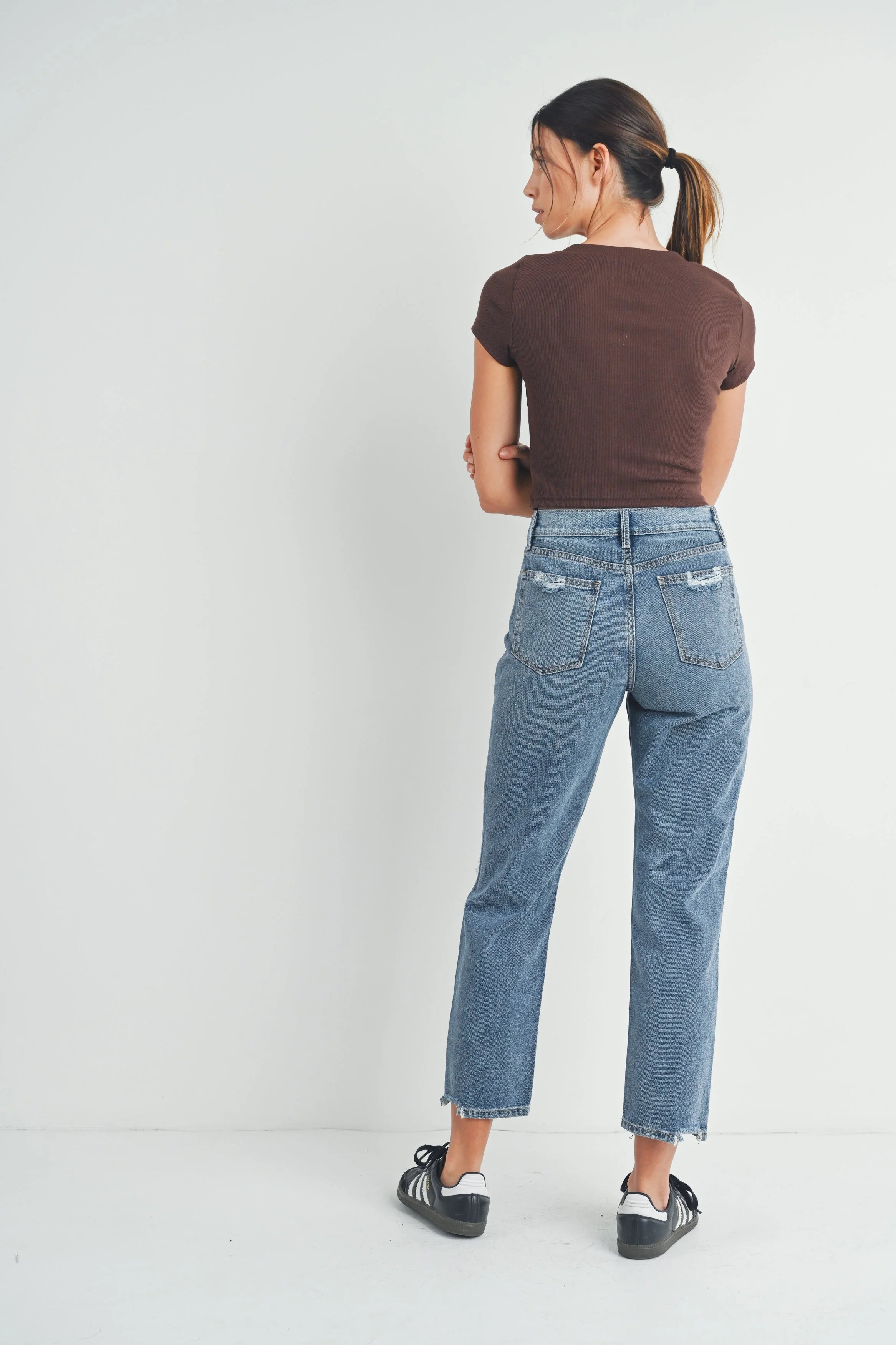 Person wearing blue jeans and a brown shirt on a white background