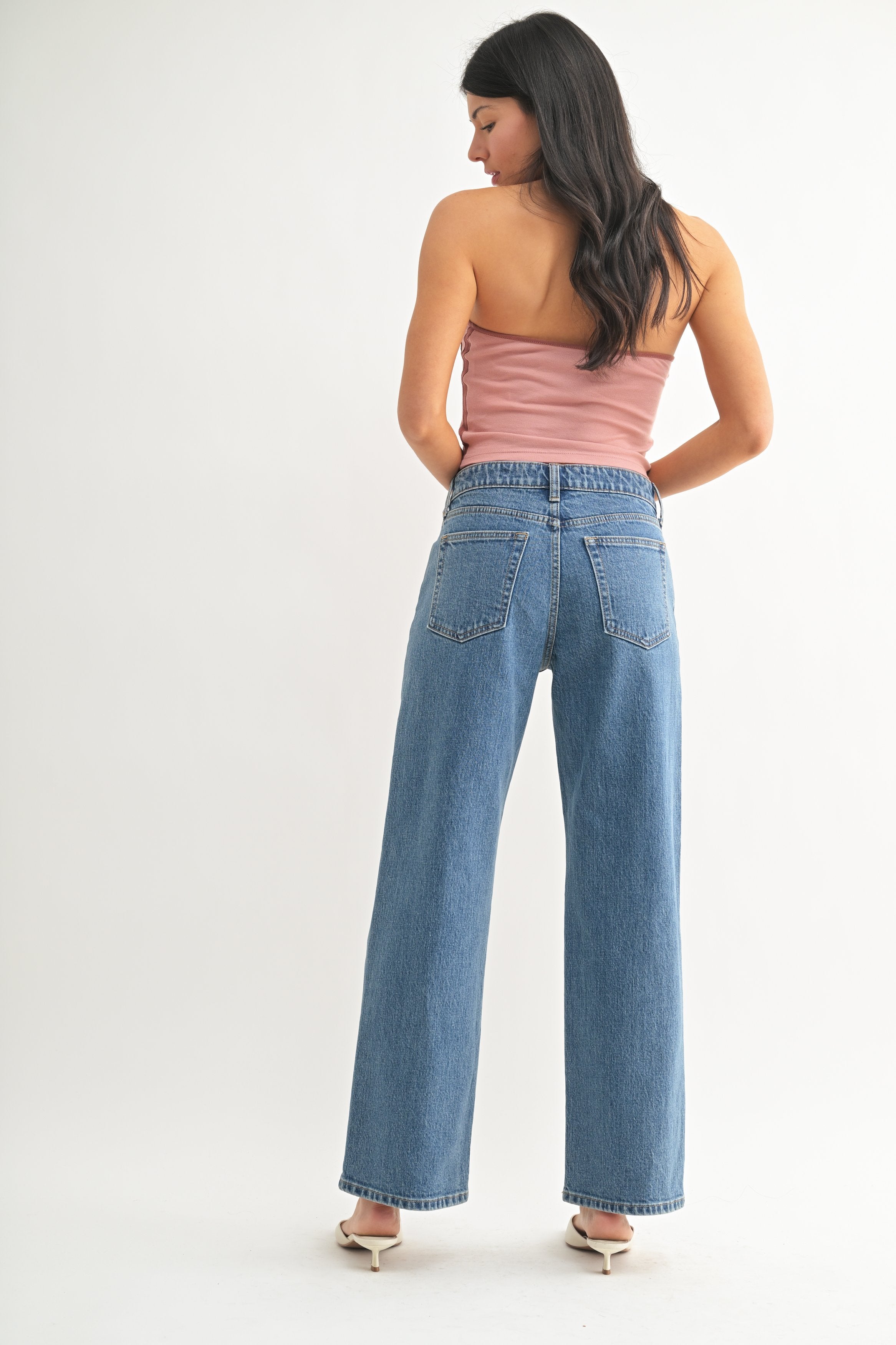 Woman wearing a pink top and blue jeans on a white background
