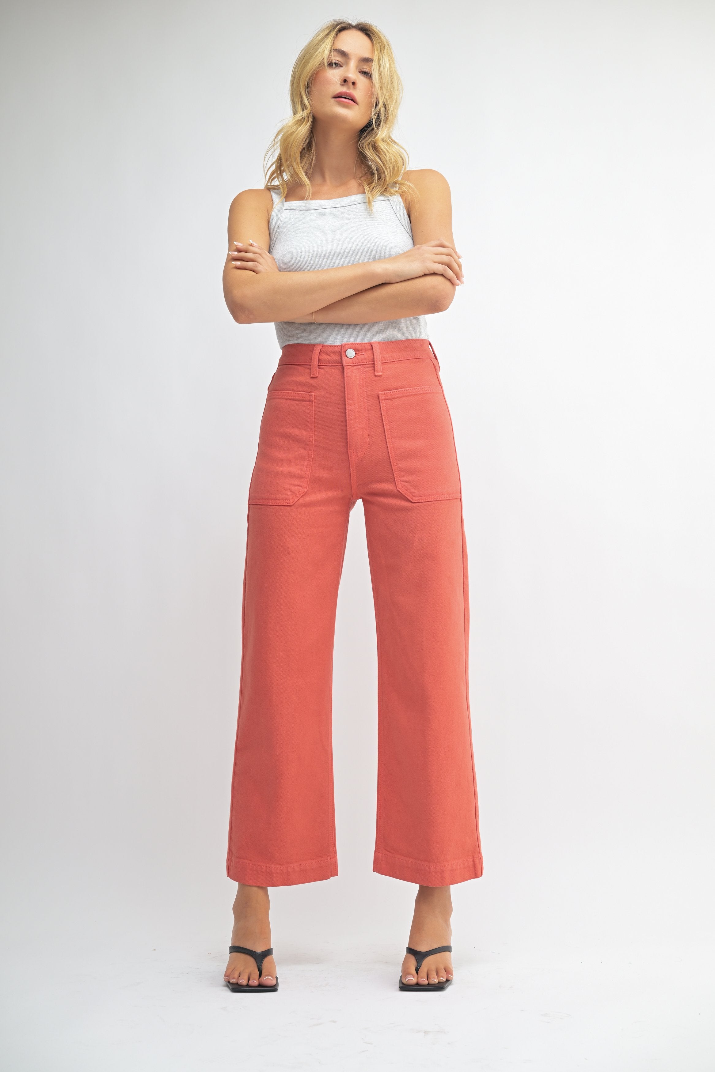 Woman wearing coral pants and a white top on a white background