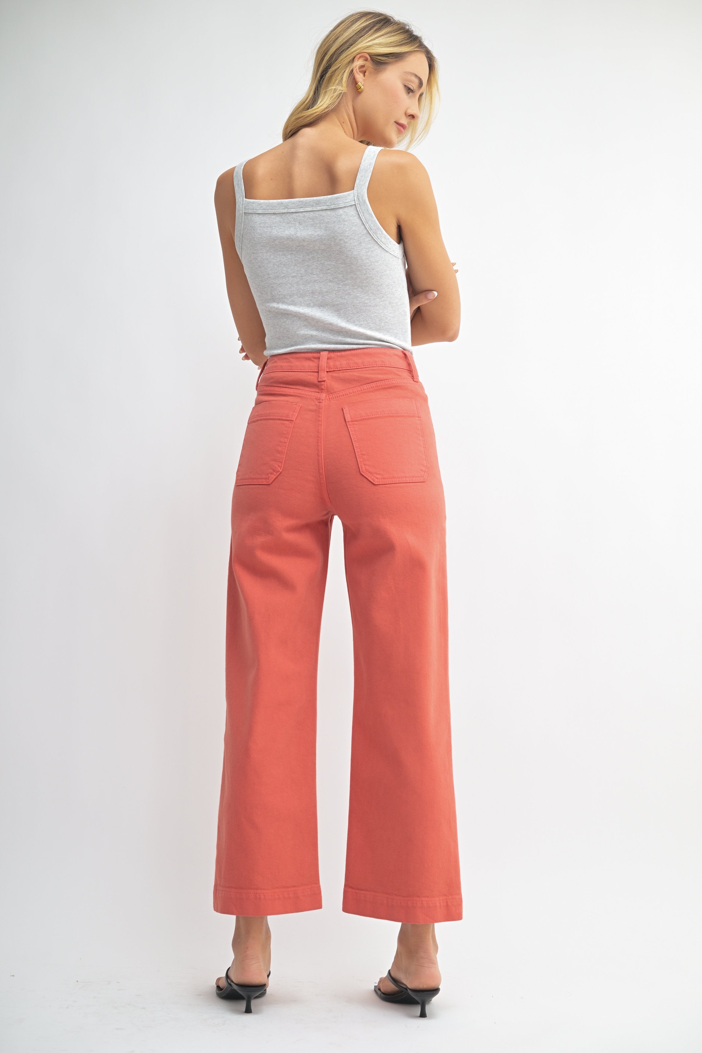 Woman wearing coral pants and a white top on a plain background