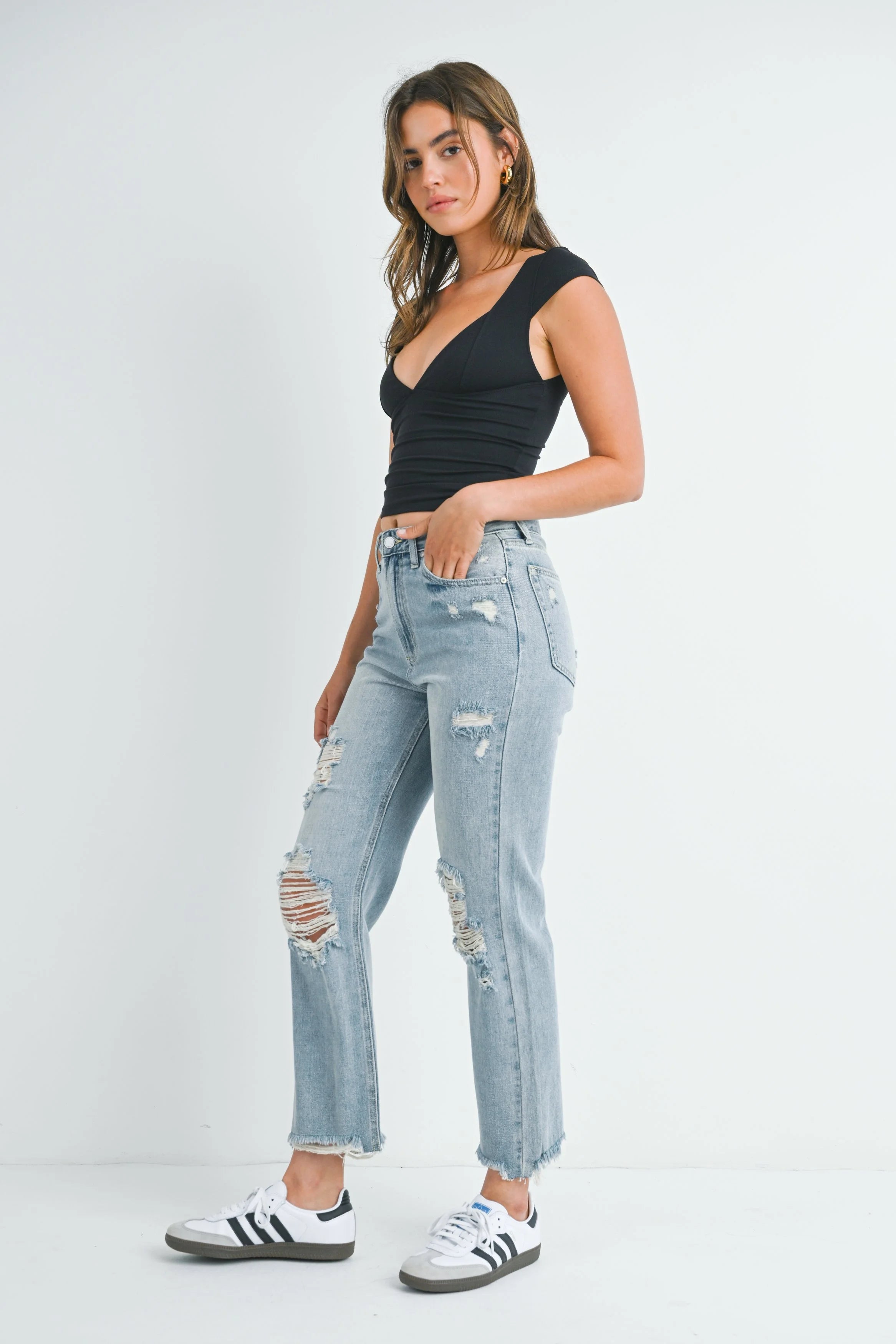 Woman wearing a black top and distressed light blue jeans on a white background