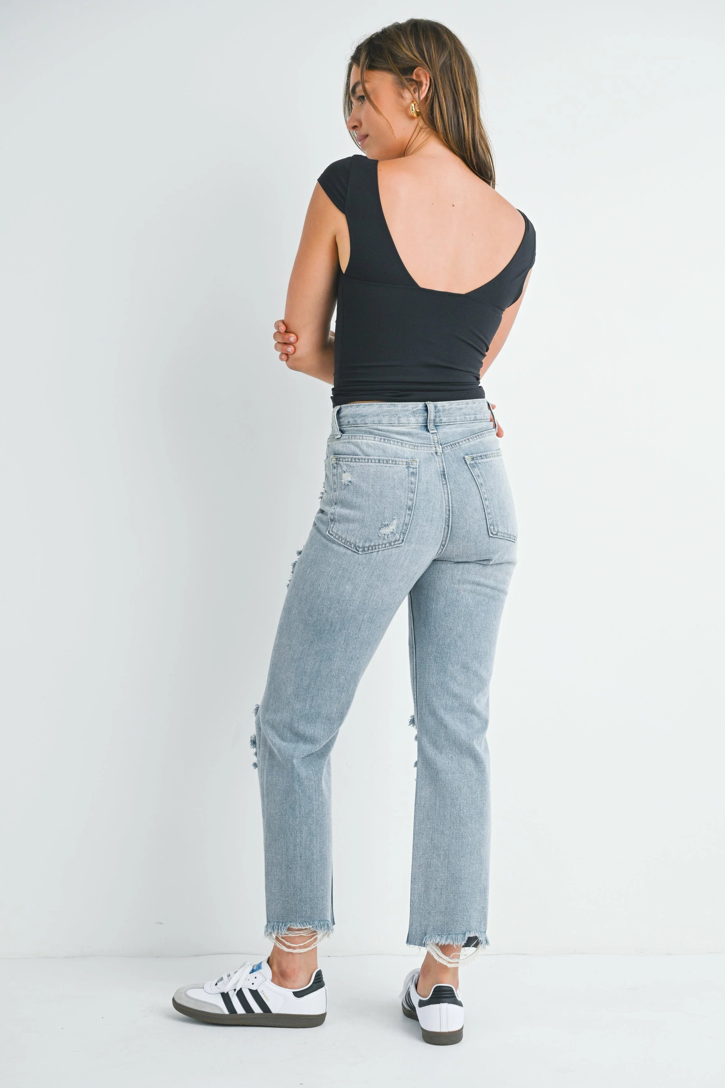 Woman wearing light blue jeans and a black top on a white background
