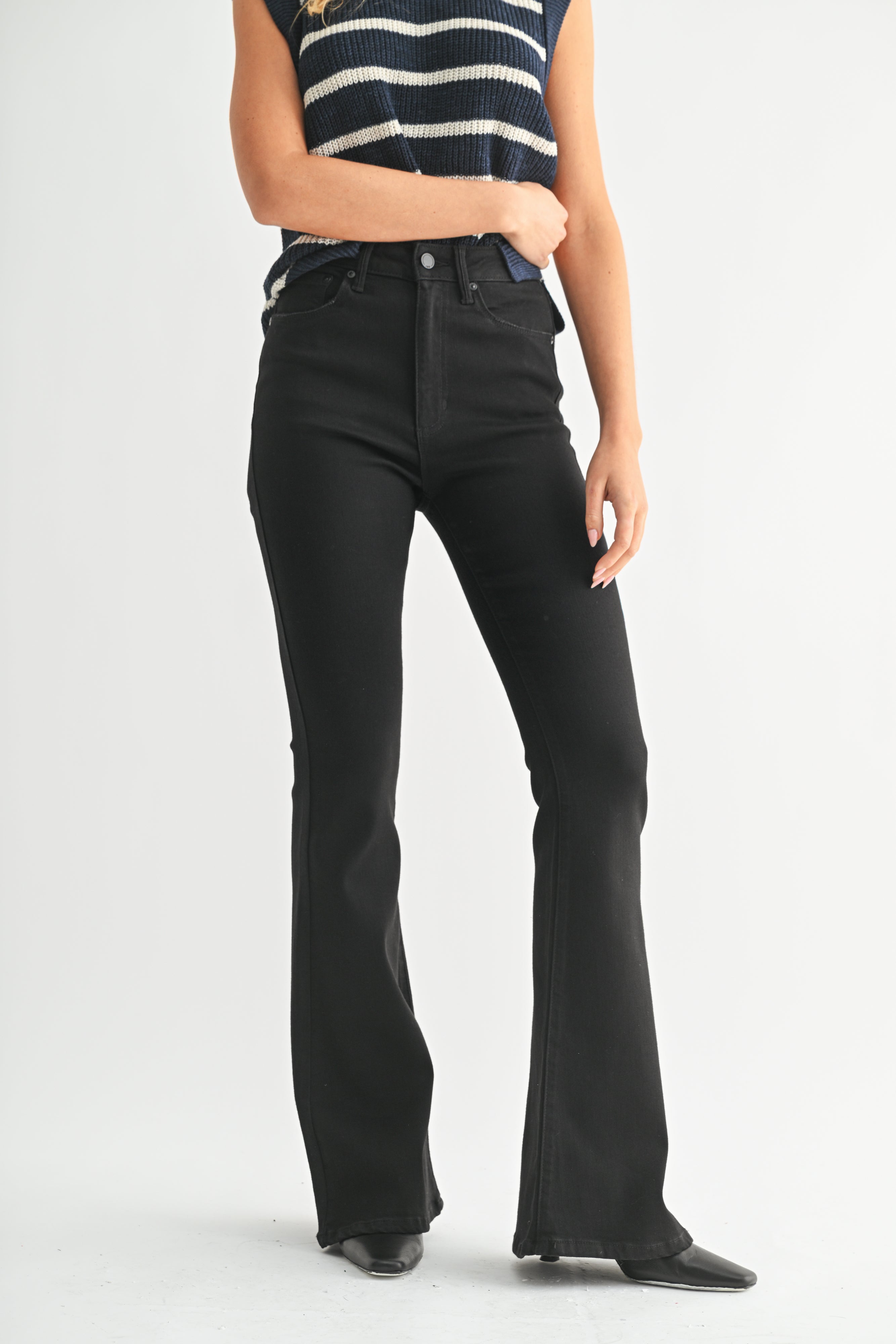 Person wearing black flared jeans and a striped top on a light gray background