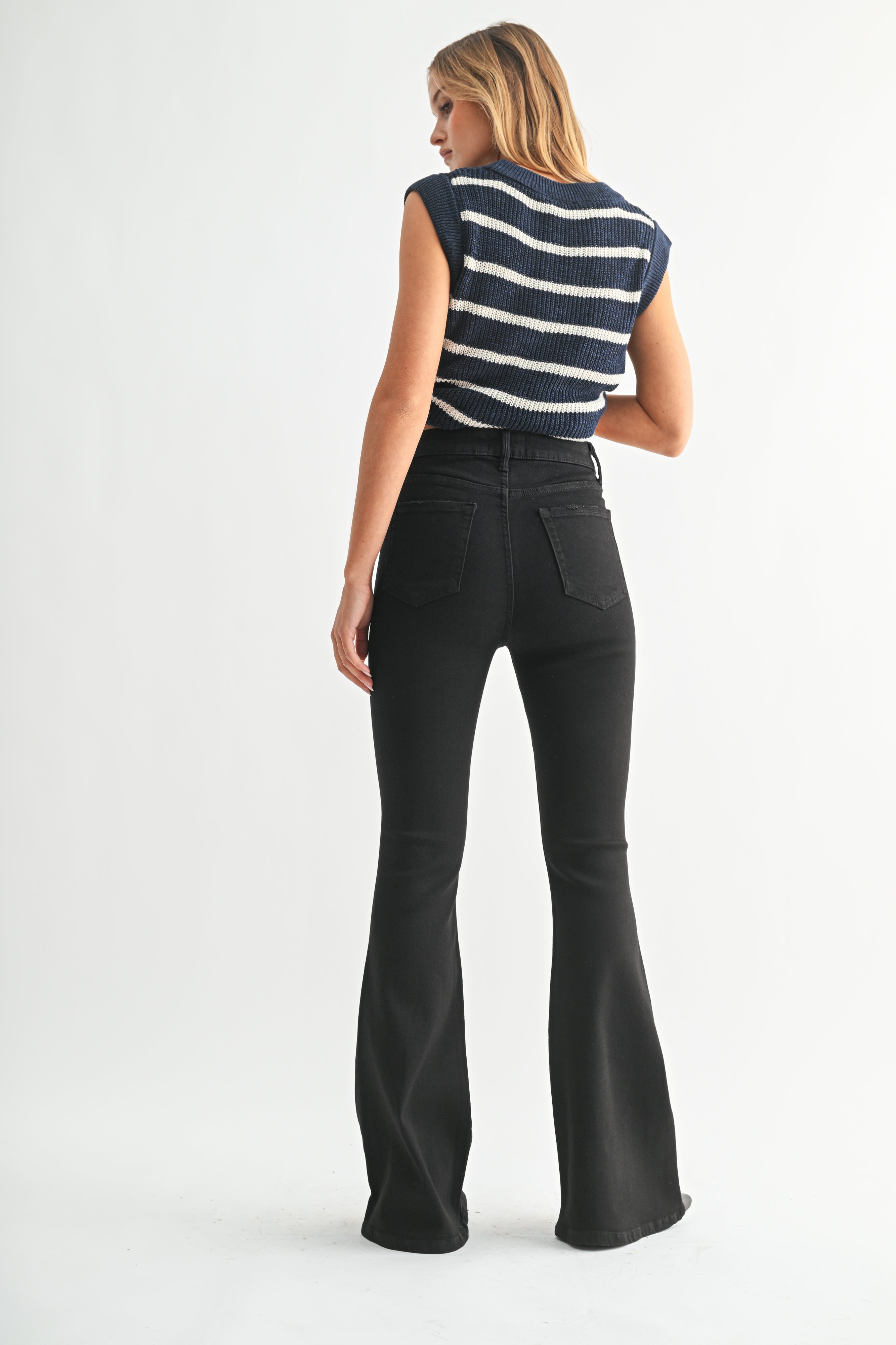 Woman wearing a striped sleeveless top and black flared jeans on a white background
