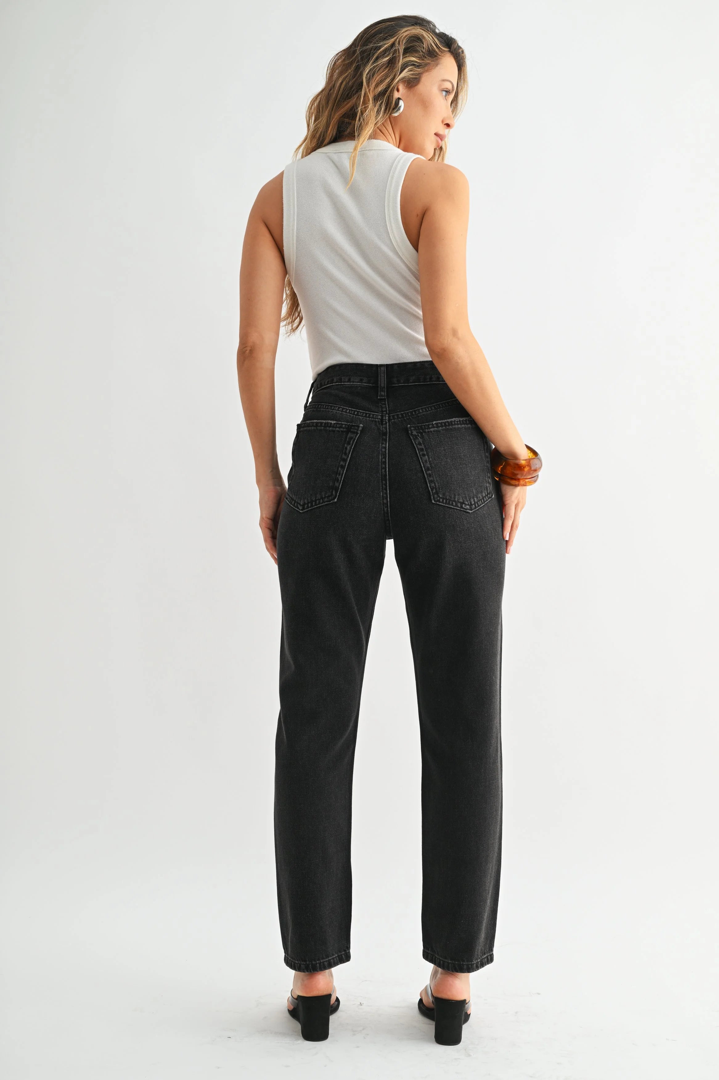 Woman wearing black high-waisted jeans and a white sleeveless top on a white background
