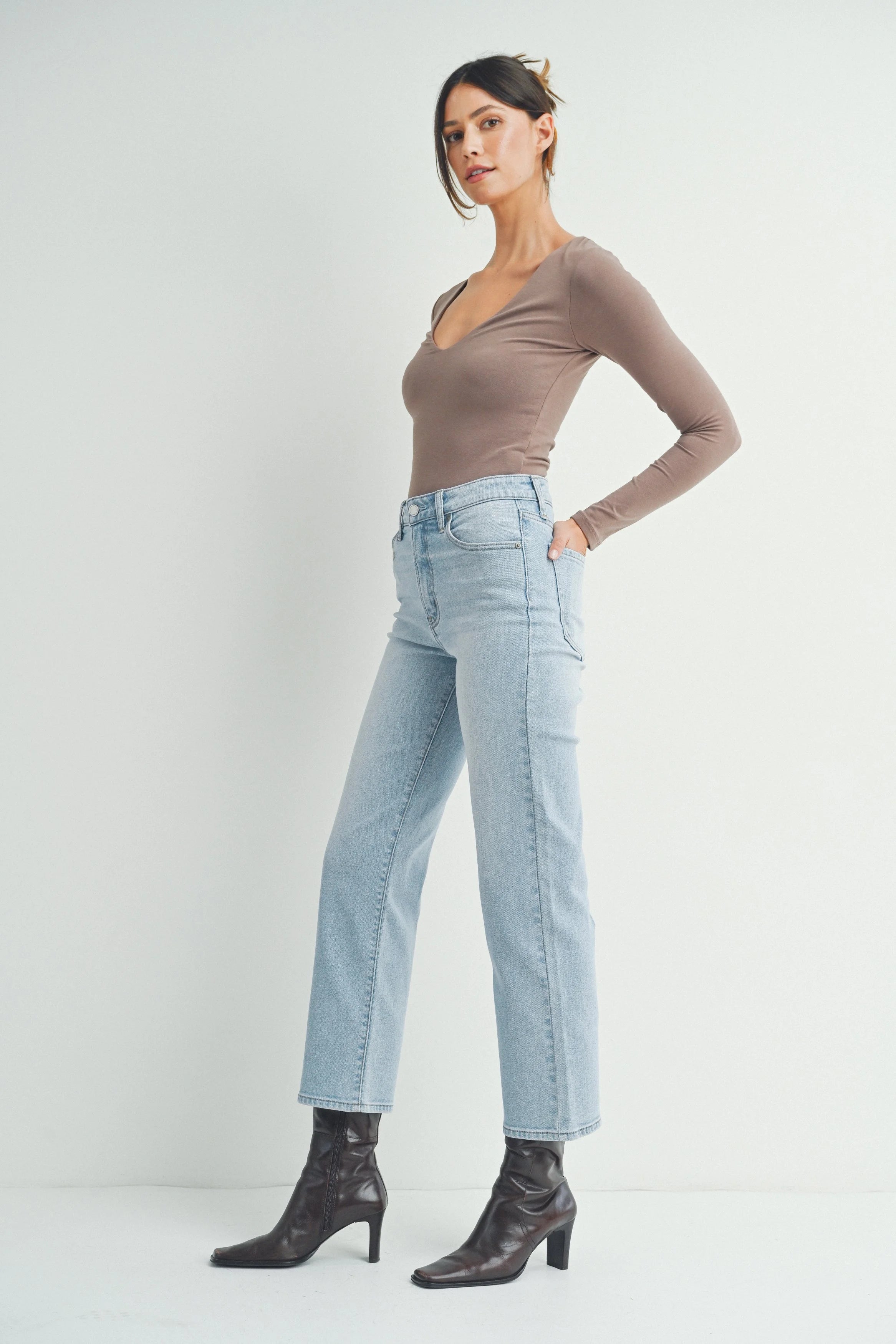 Woman wearing a brown long-sleeve top and light blue jeans on a white background