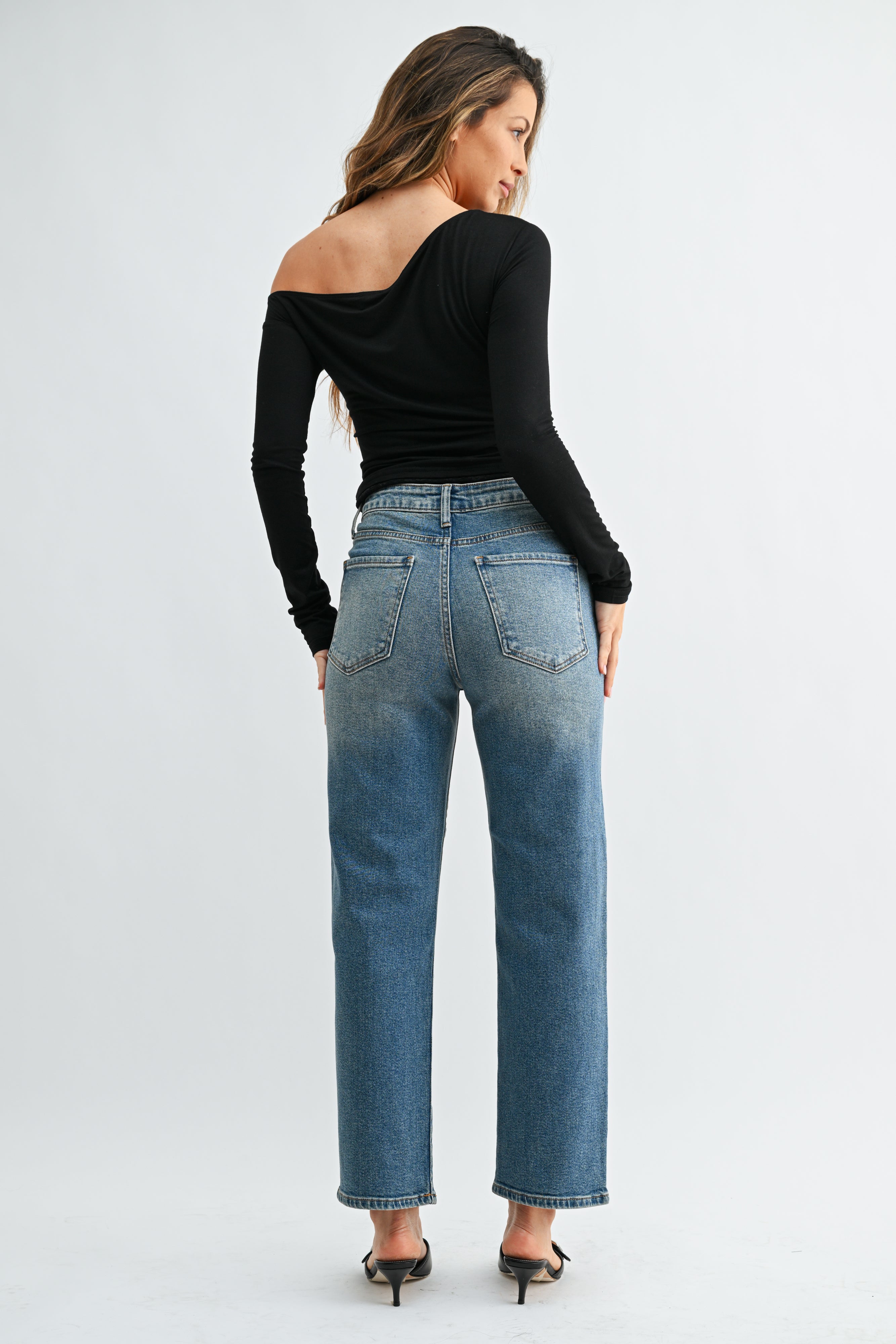 Woman wearing blue jeans and a black top on a white background