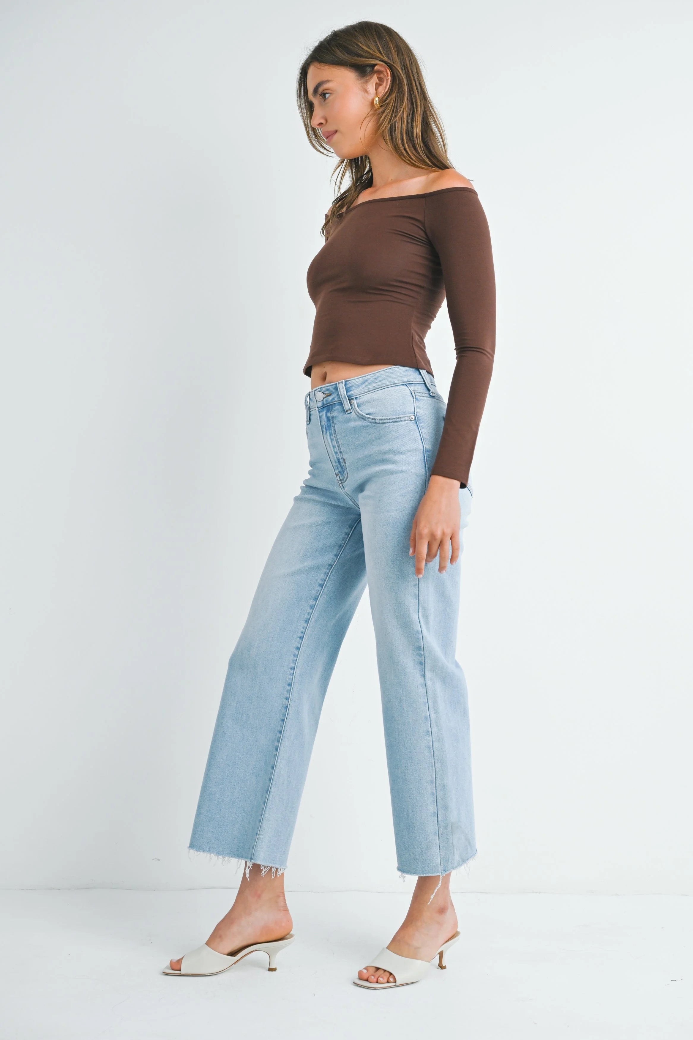 Woman wearing a brown off-shoulder top and light blue jeans on a white background