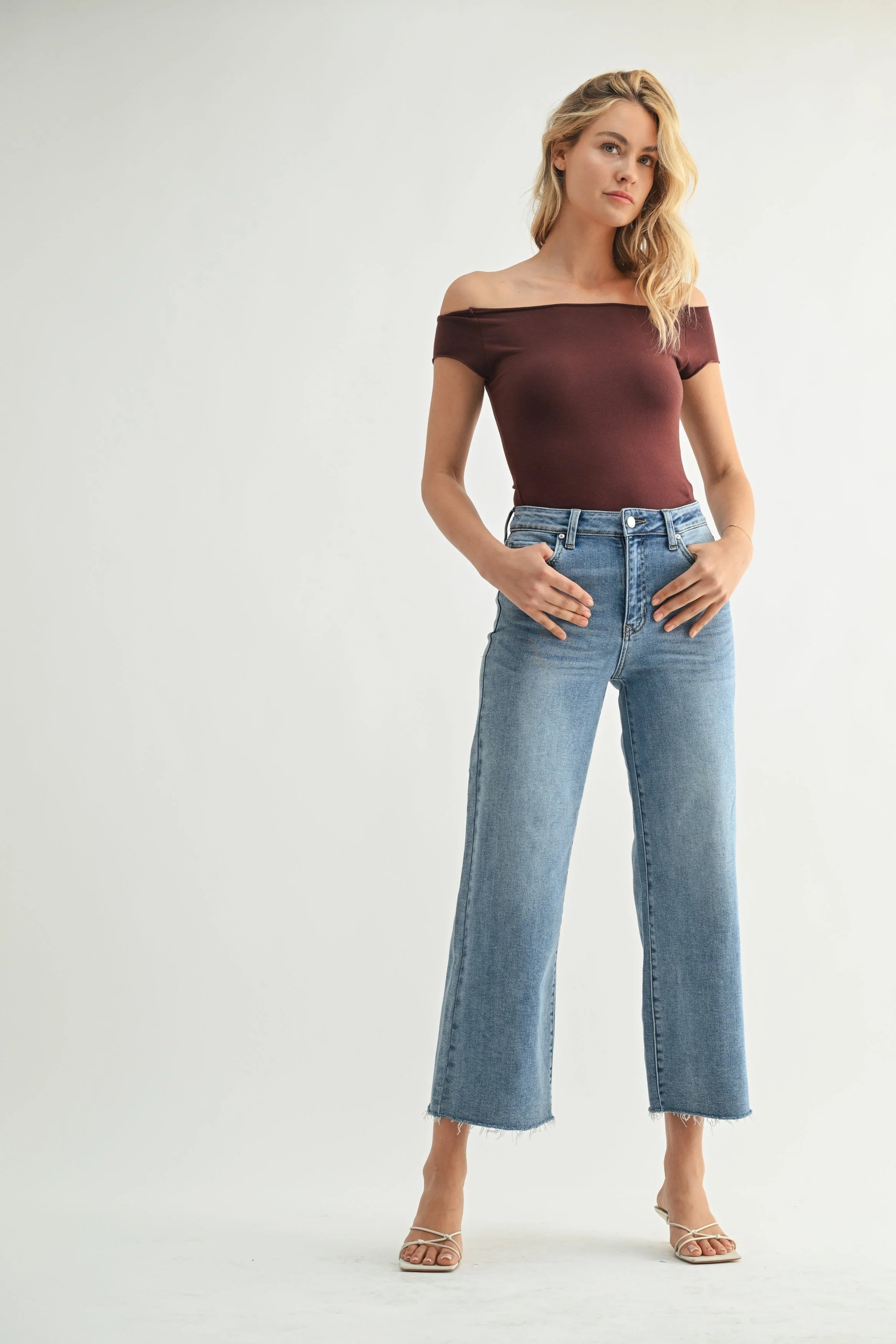 Woman wearing a brown off-shoulder top and blue jeans on a white background