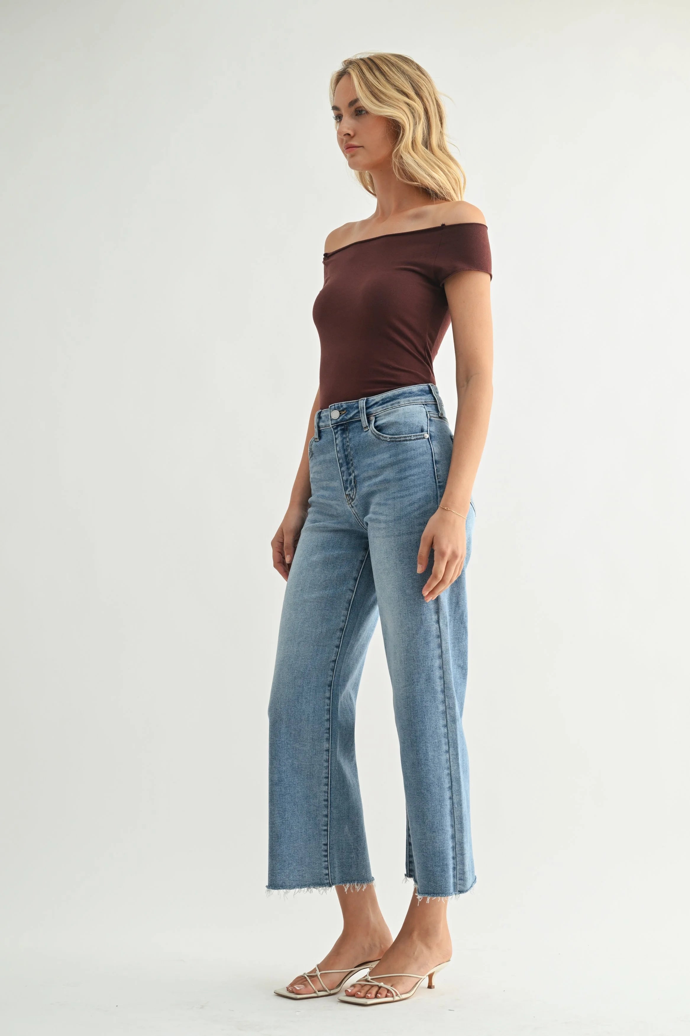 Woman wearing a brown off-shoulder top and light blue jeans on a white background