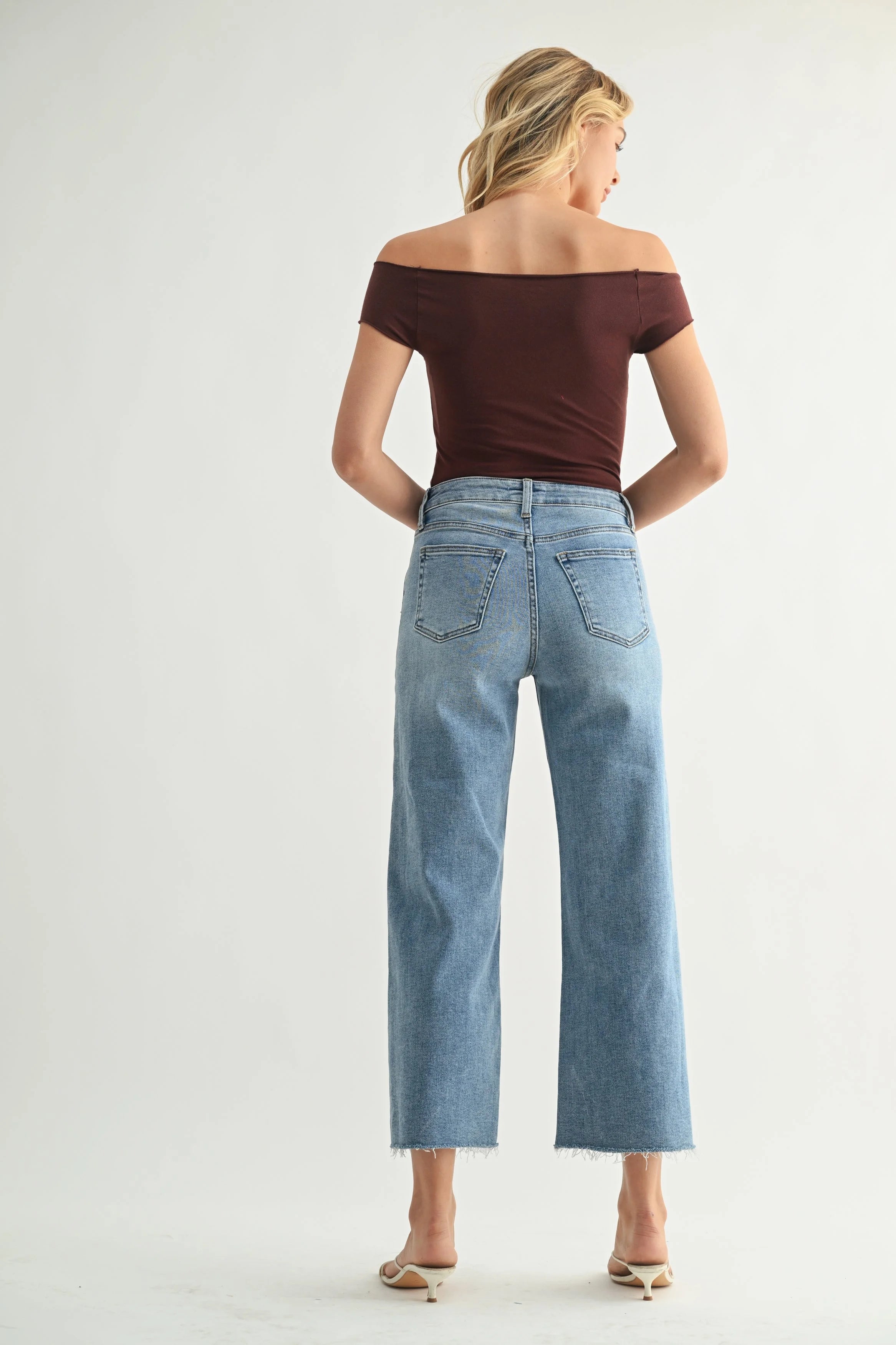 Woman wearing a brown off-shoulder top and light blue jeans on a white background