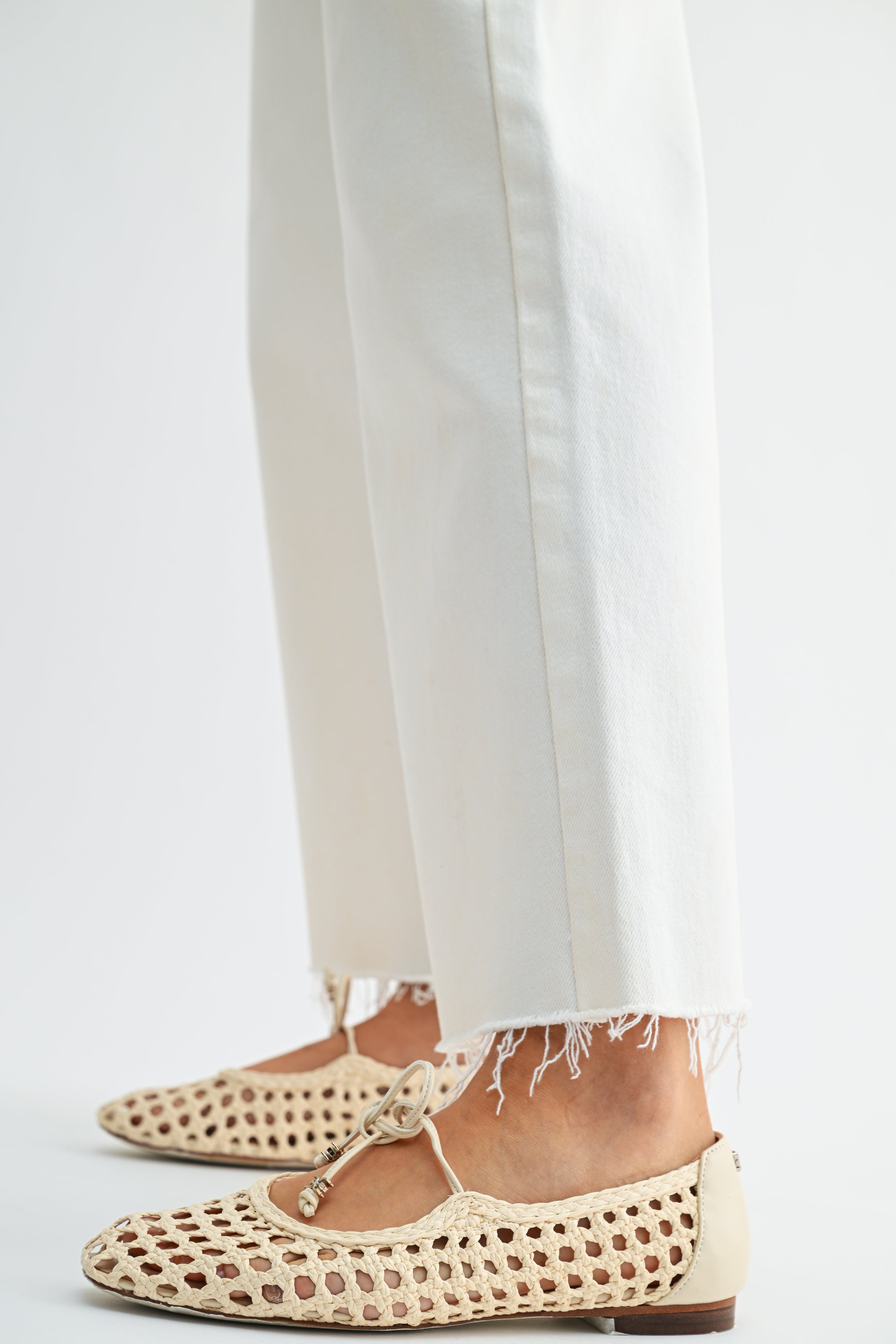 Beige perforated flats worn with white pants on a light gray background