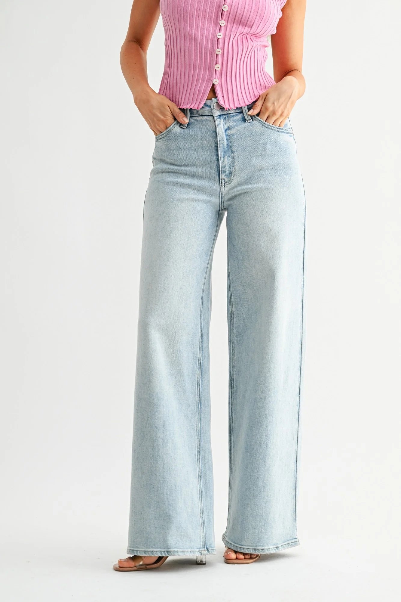 Person wearing light blue wide-leg jeans and a pink button-up shirt on a white background