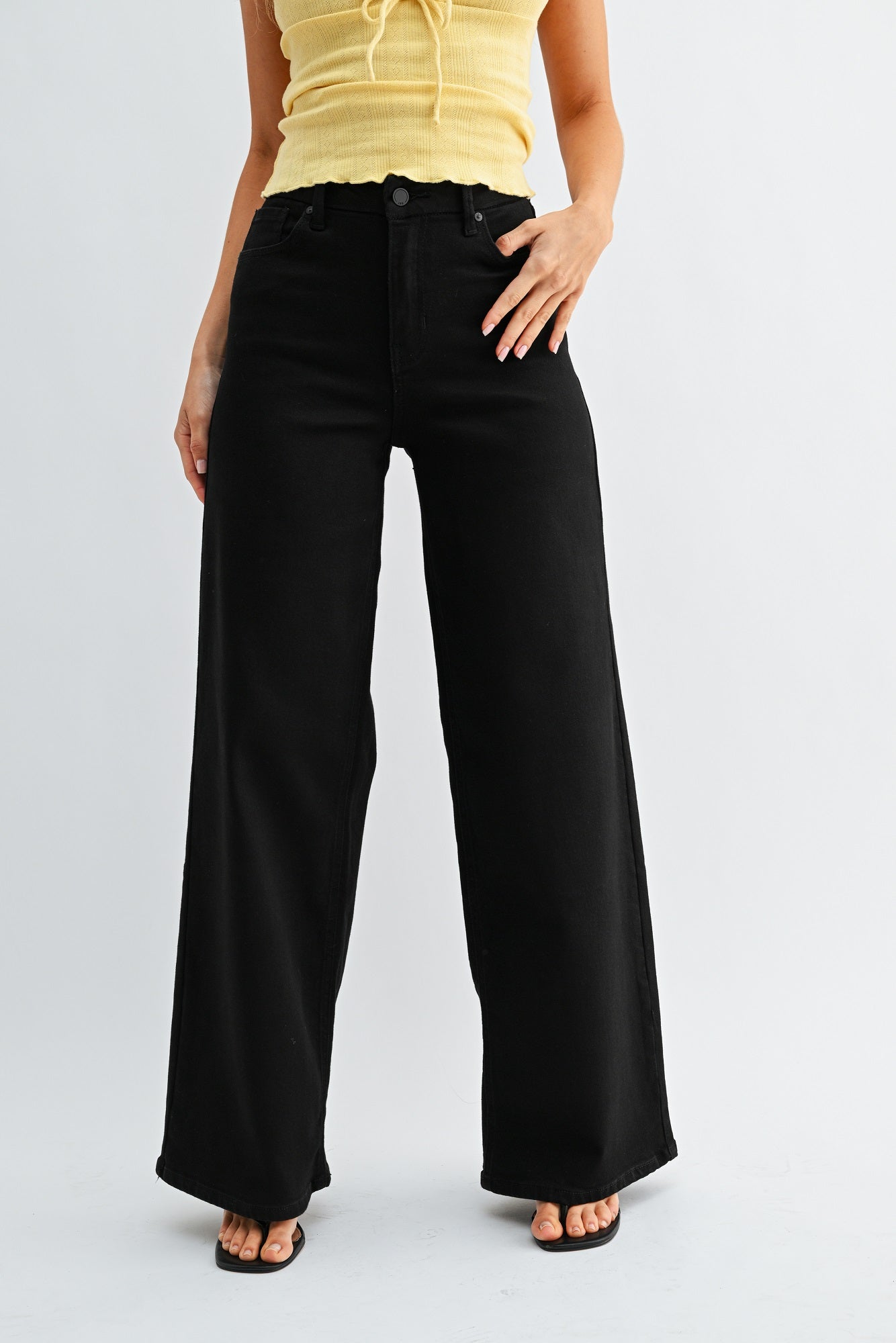 Person wearing black wide-leg jeans and a yellow top on a white background