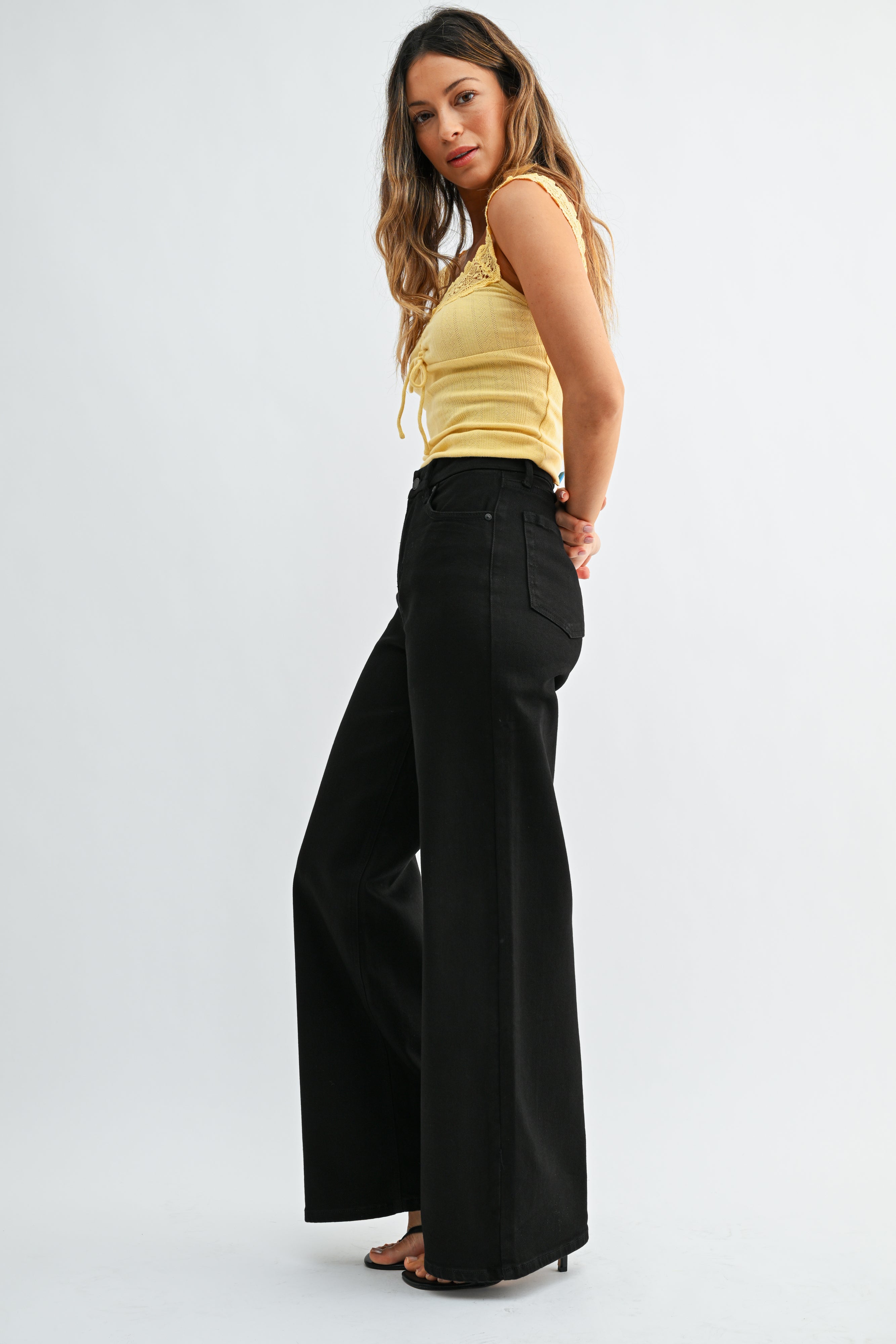 Woman wearing a yellow top and black wide-leg pants on a white background