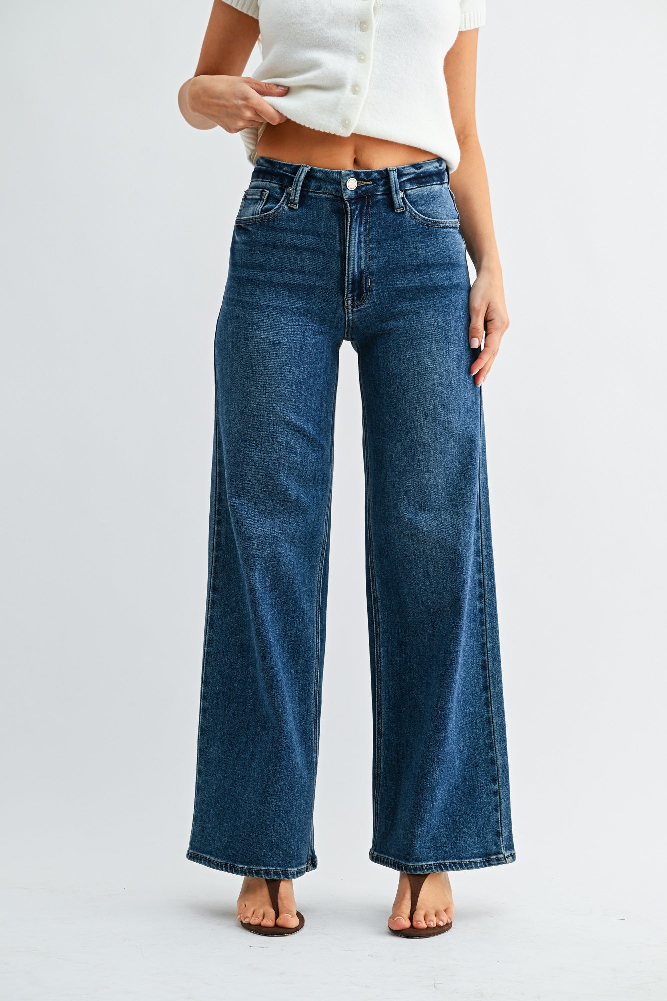 Person wearing blue jeans and a white top on a light gray background