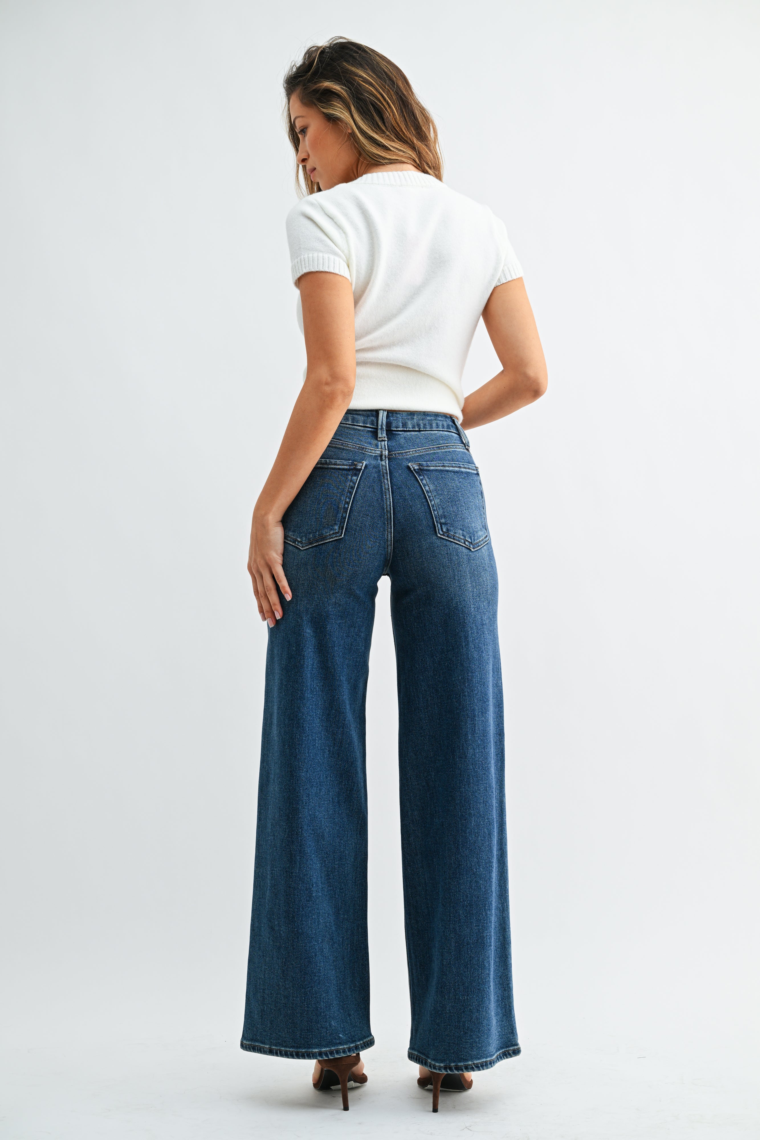Person wearing blue jeans and a white top on a plain background