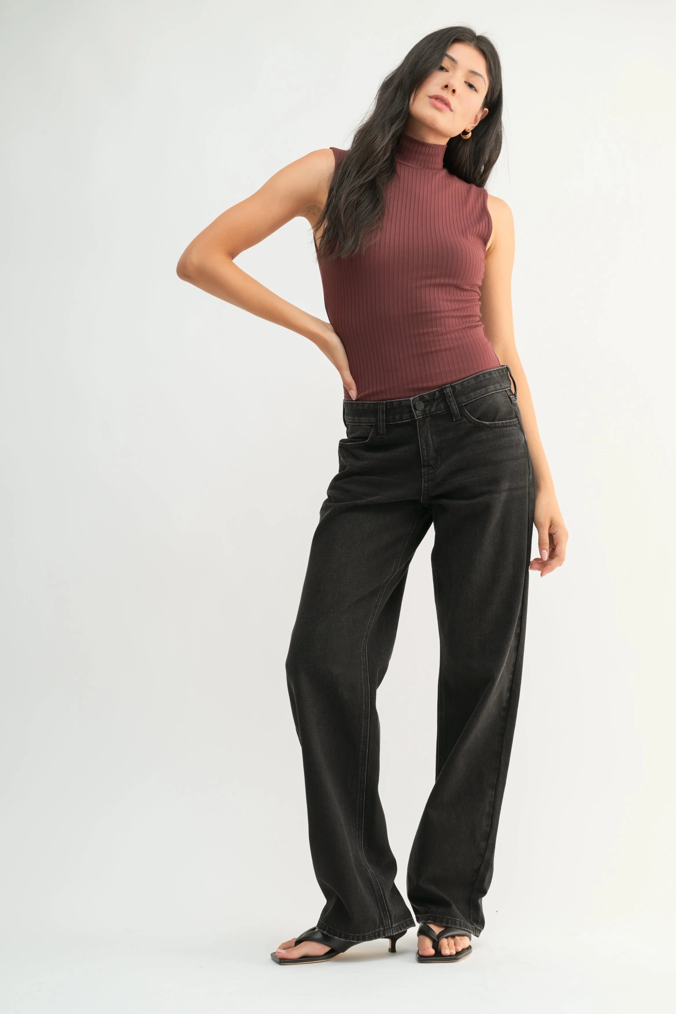Woman wearing a brown ribbed tank top and black high-waisted jeans on a white background