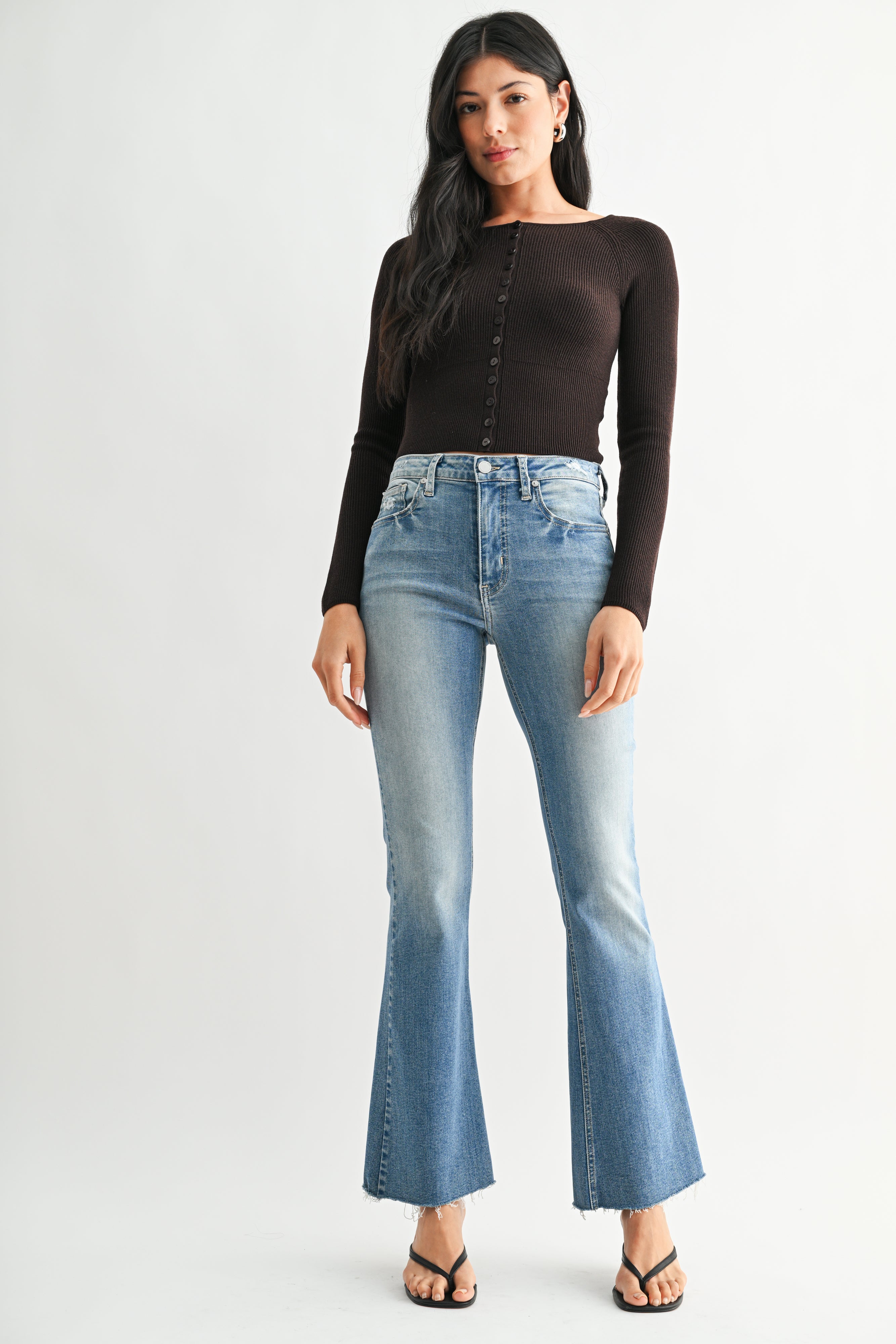Woman wearing a black long-sleeve top and light blue flared jeans on a white background