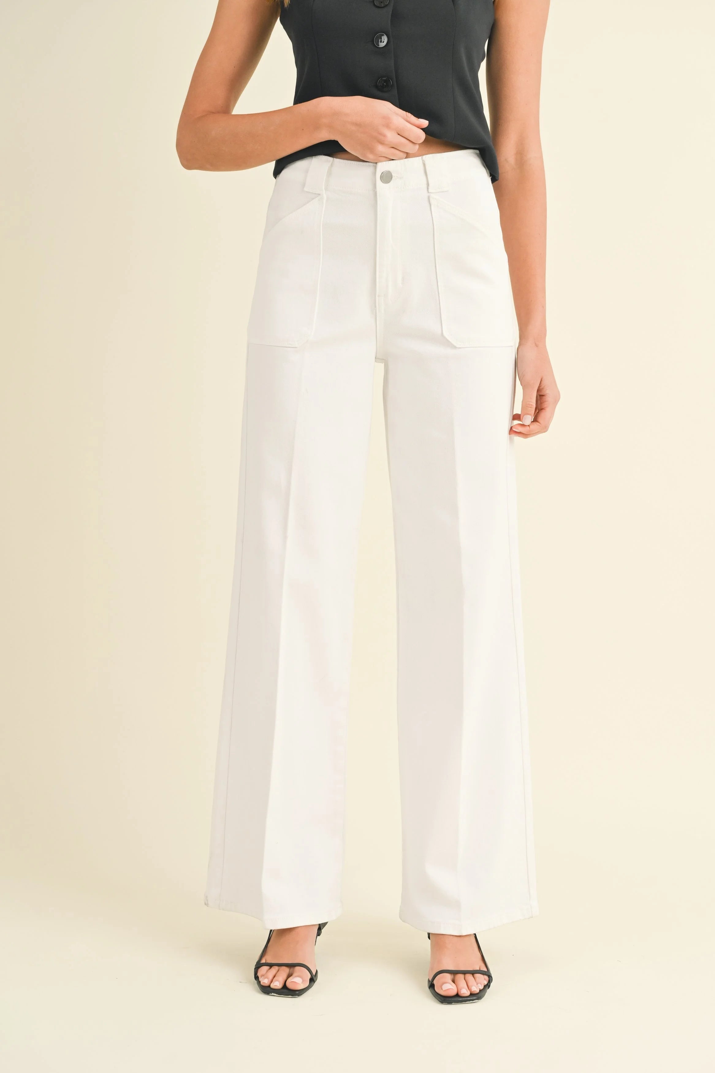 Person wearing white wide-leg pants and a black top on a beige background