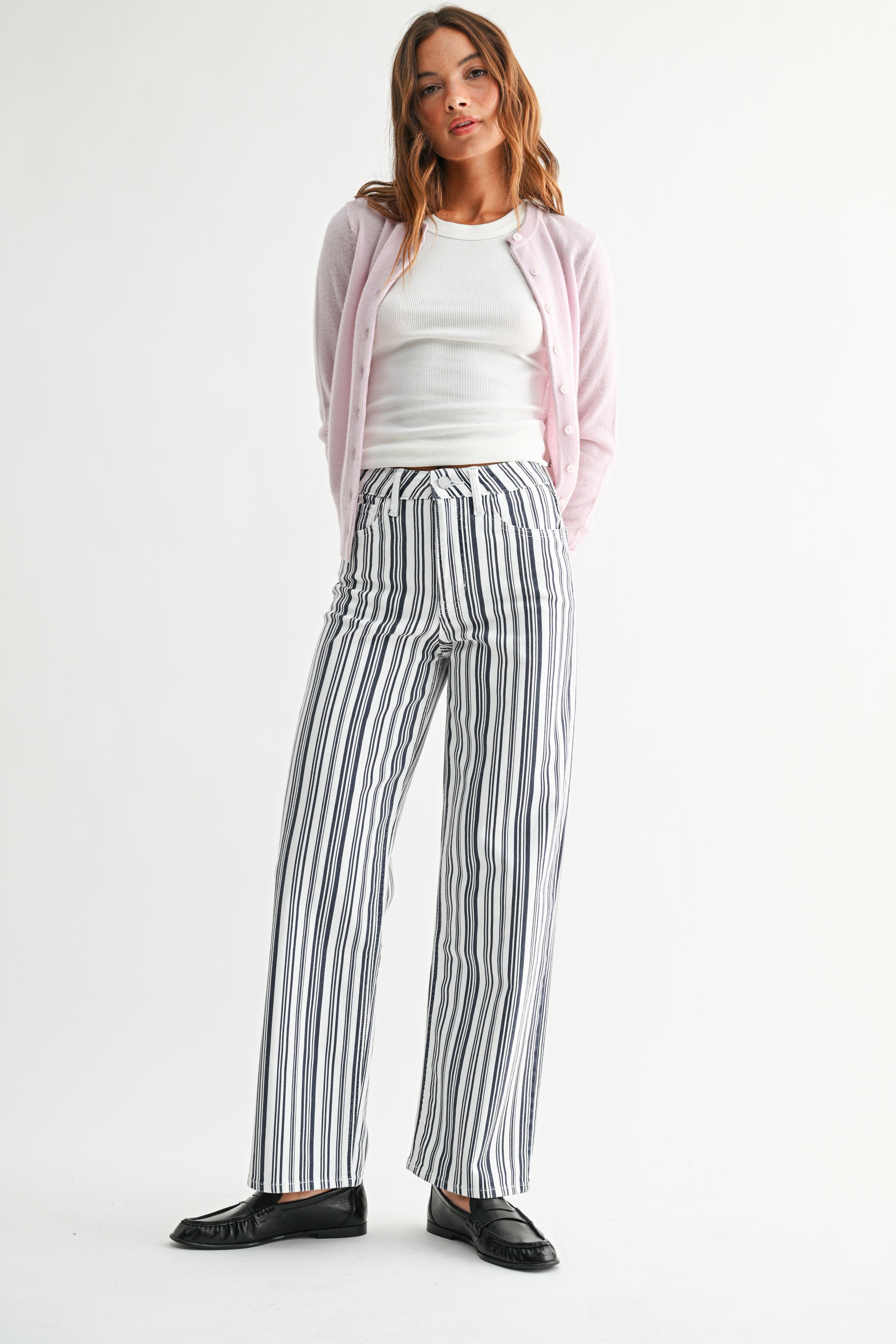 Woman wearing a pink cardigan, white top, and striped pants on a white background