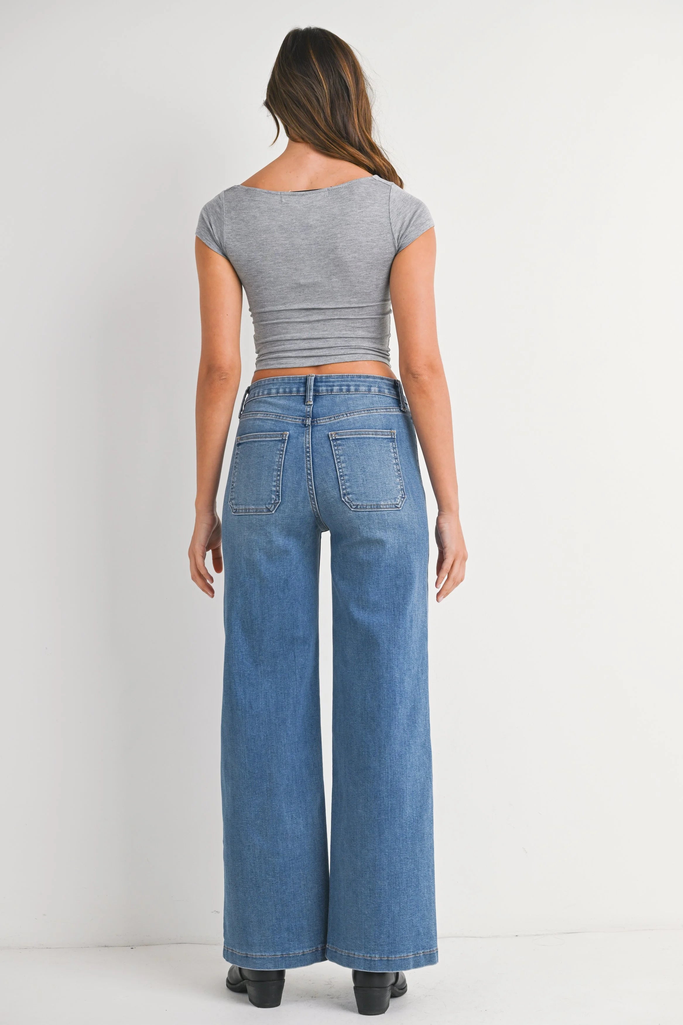 Woman wearing a gray crop top and blue wide-leg jeans on a white background