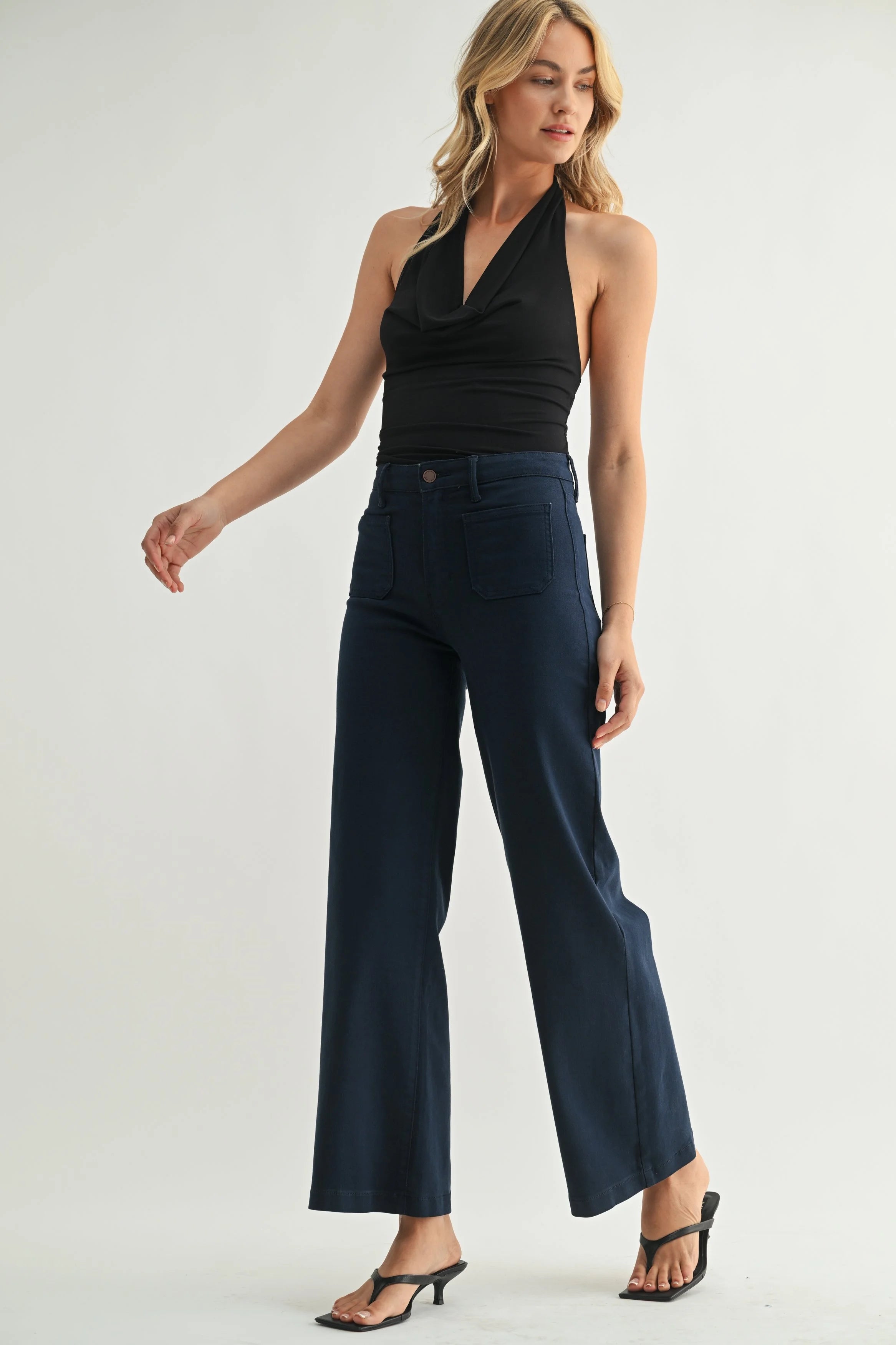 Woman wearing a black halter top and navy wide-leg pants on a white background