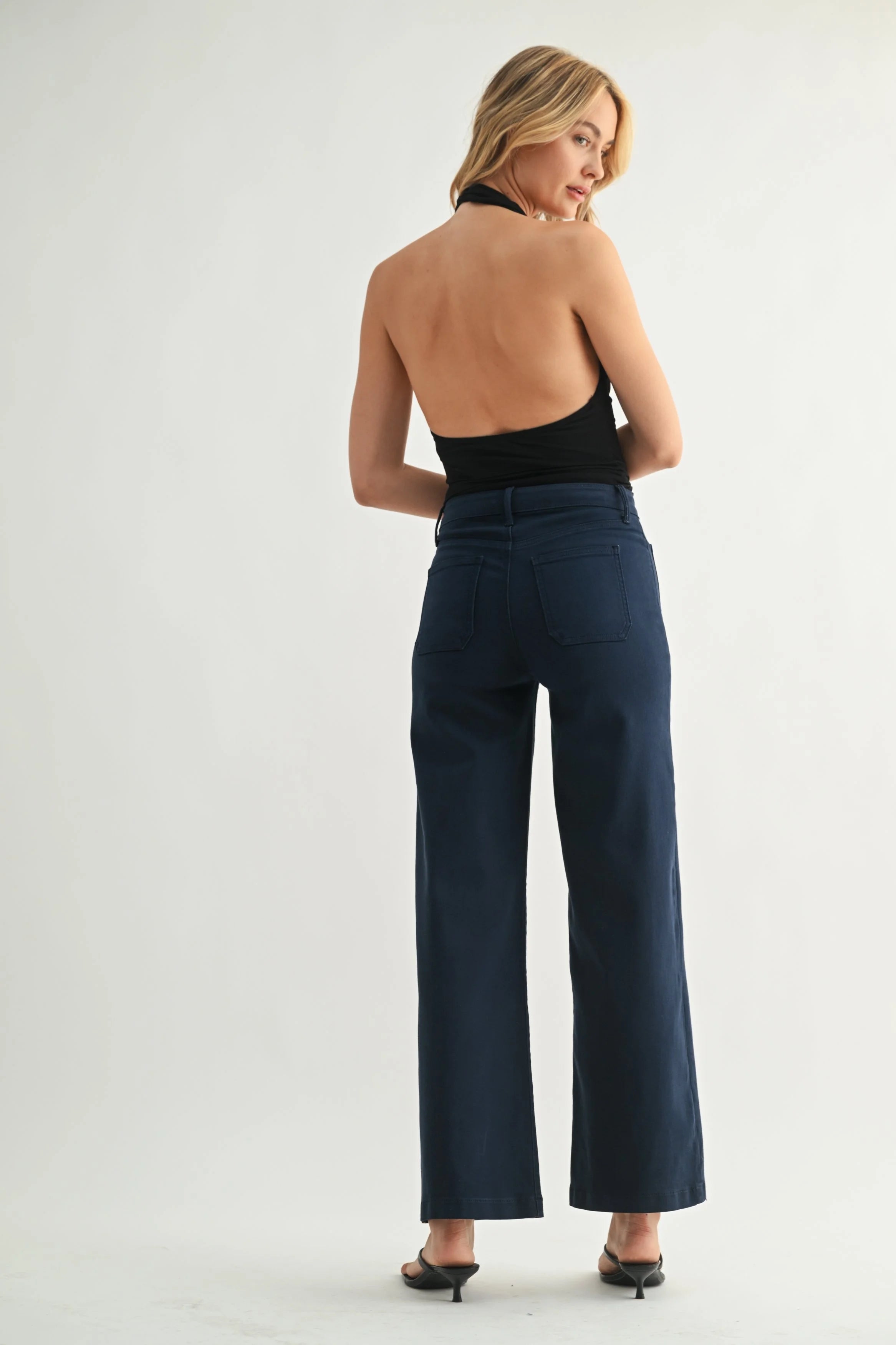 Woman wearing a black halter top and blue high-waisted pants on a white background